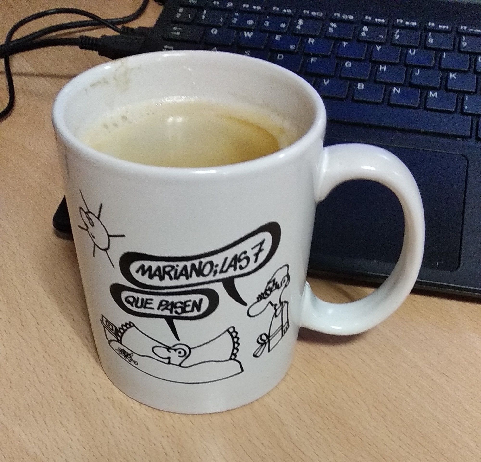 Taza blanca llena de café, con dibujo de Forges:
Ella dice "Mariano; las 7".
El, acostado, responde "Que pasen".
Detrás se ve el teclado de un portátil.