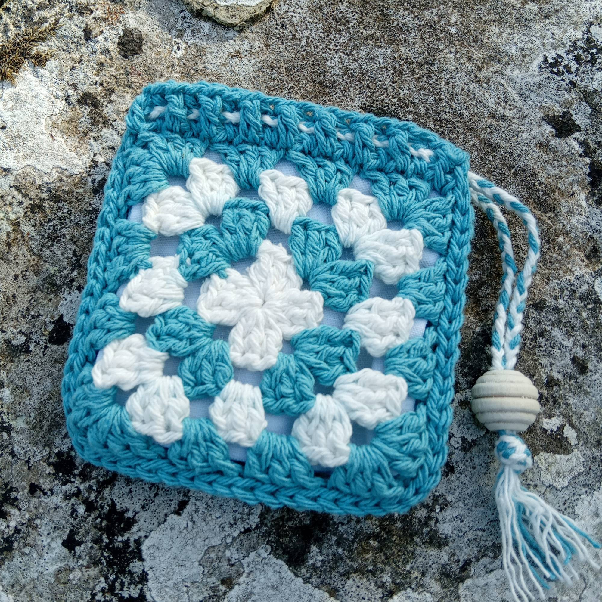 Pochette granny square vert et blanc avec un lien de serrage.