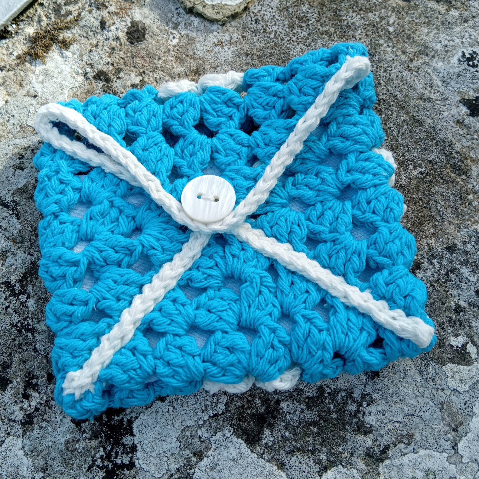 Pochette granny square turquoise et blanc avec un bouton.