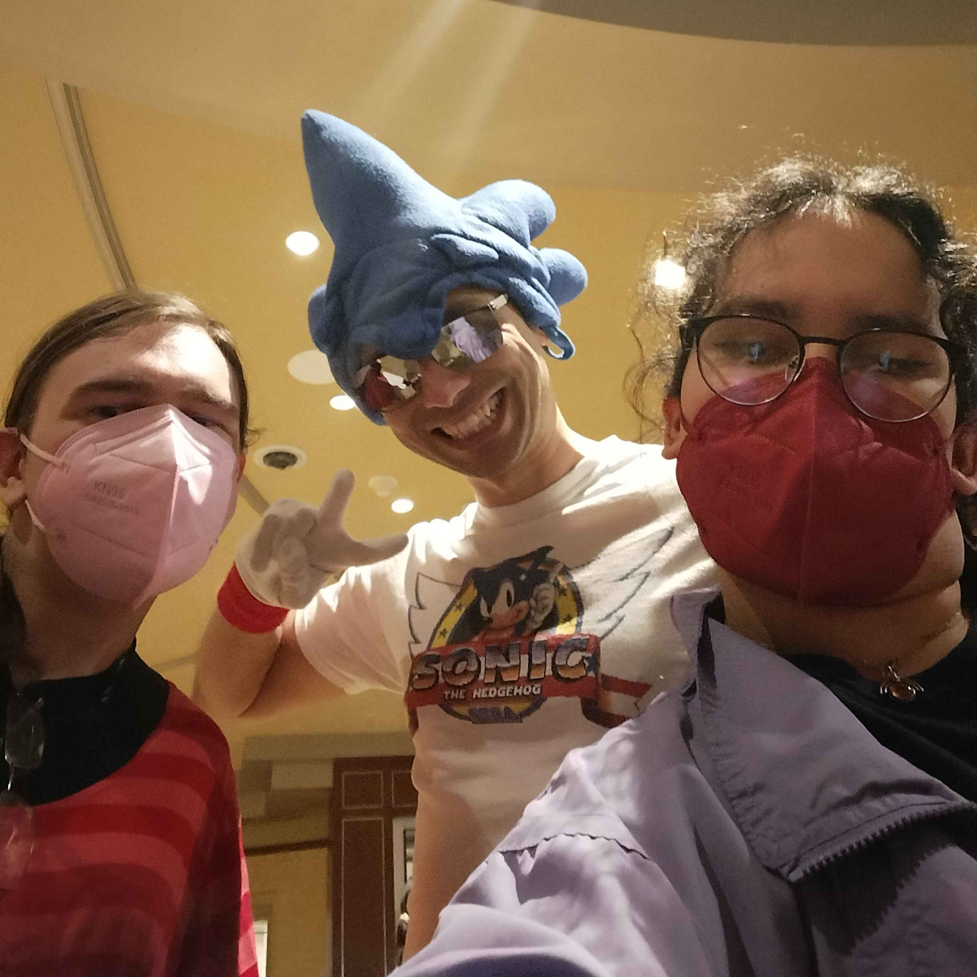 two women on each side of the photo, with a person in the middle posing, dressed as "sonicman" from sonic the hedgehog 2006