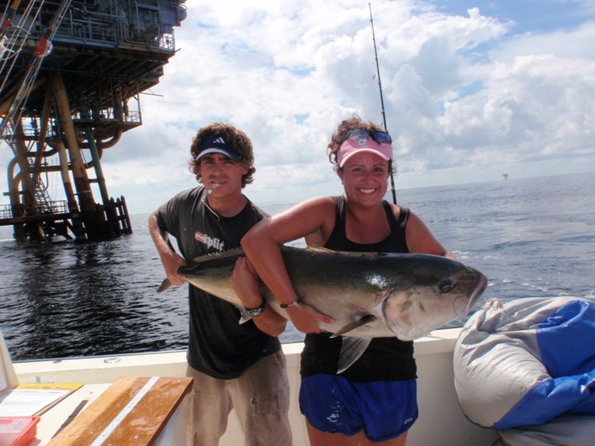 Man and woman on a boat holding a large greater amberjack. The fish is so large it takes two of them to hold it.