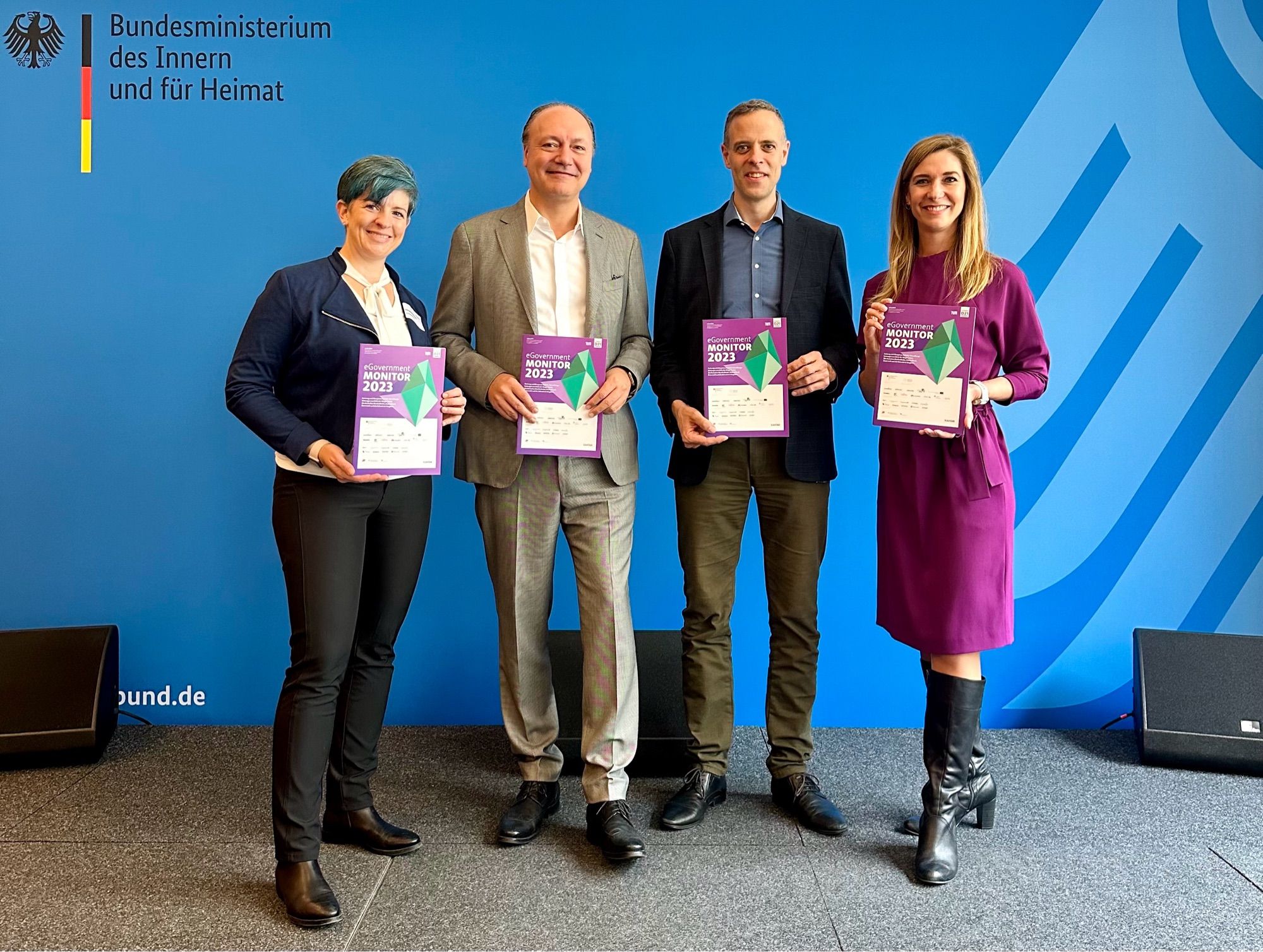 Christiane Fritsch, Marc Reinhardt, Markus Rochter und Lena-Sophie Müller vor einem Foto-Hintergrund des BMI. Alle haben eine Ausgabe des eGovernment MONITOR in der Hand.