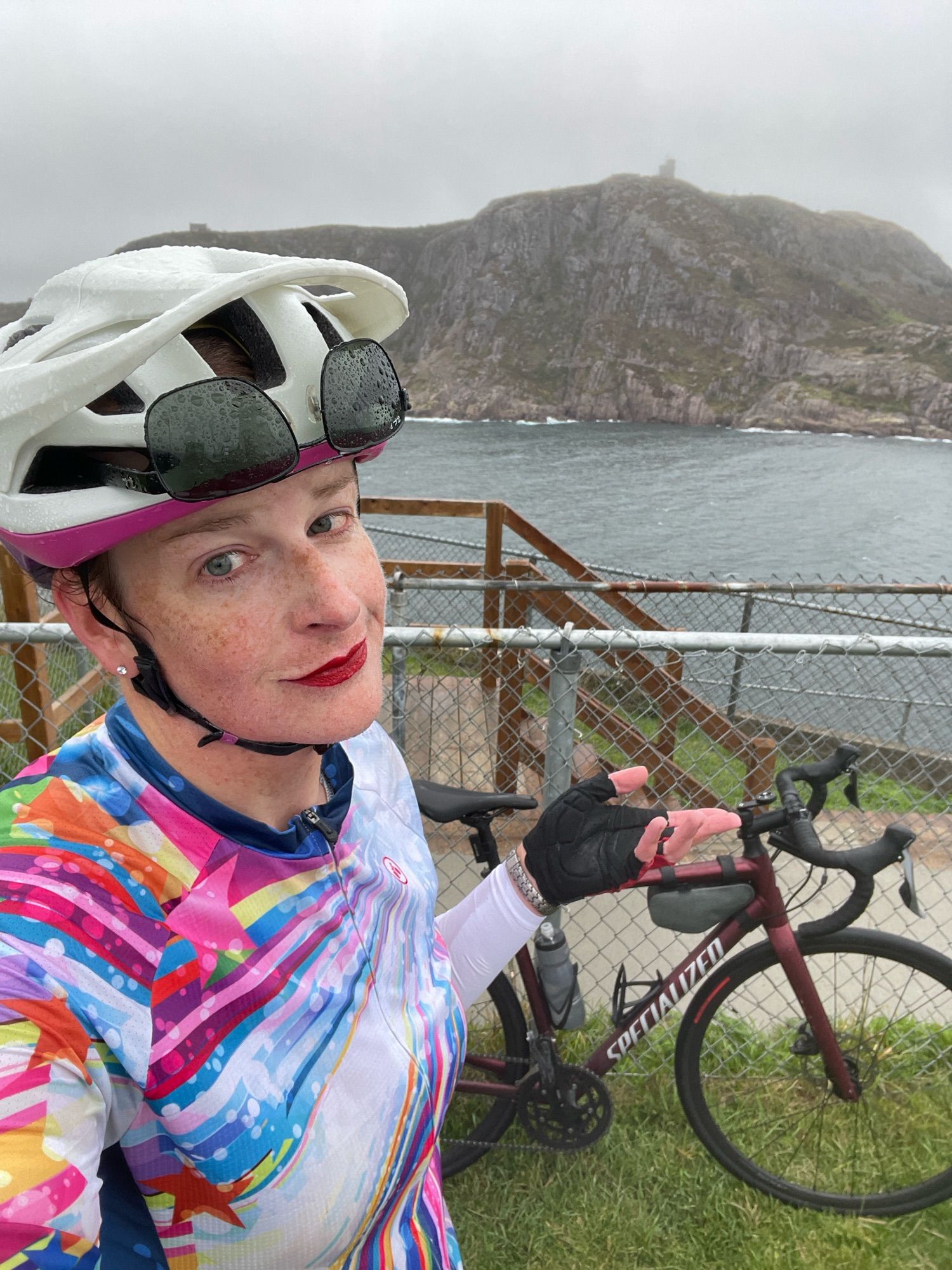 Cailín is standing at the end of the trail at Fort Amherst. She is very wet. Behind her perking through the fog is Cabot Tower on top of Signal Hill, the narrows leading into St. John’s harbour, and her bike.