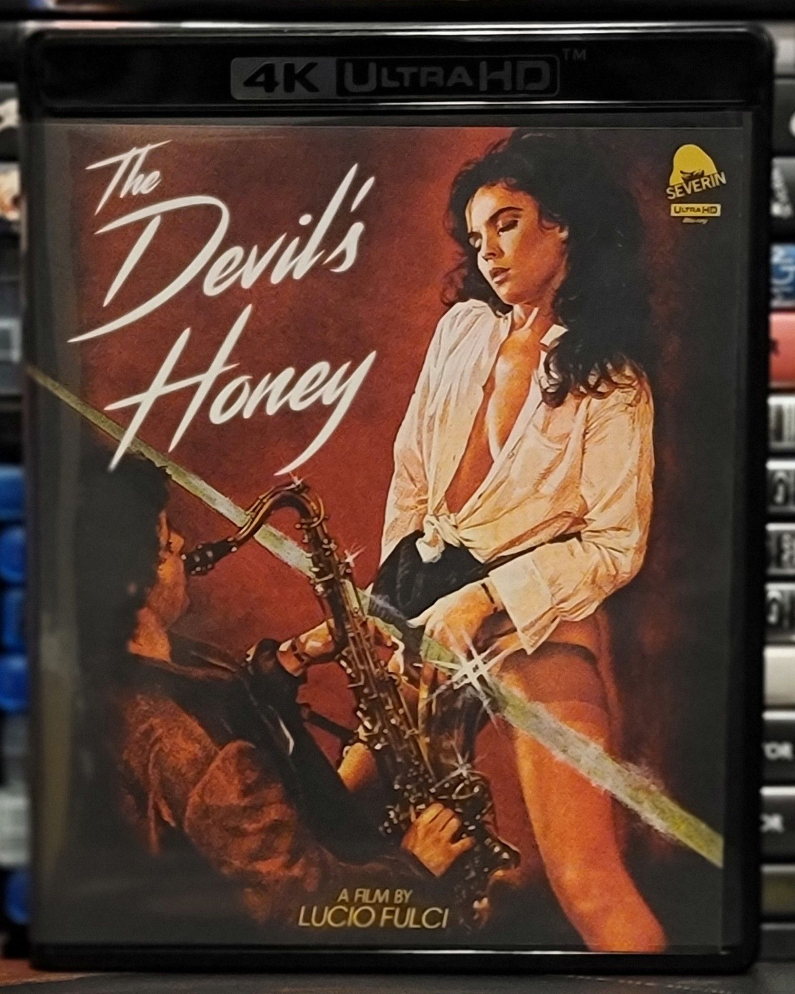 Blu ray cover for The Devil's Honey. It shows a woman in front of a saxophone player. She looks like she's having quite the ecstatic moment.