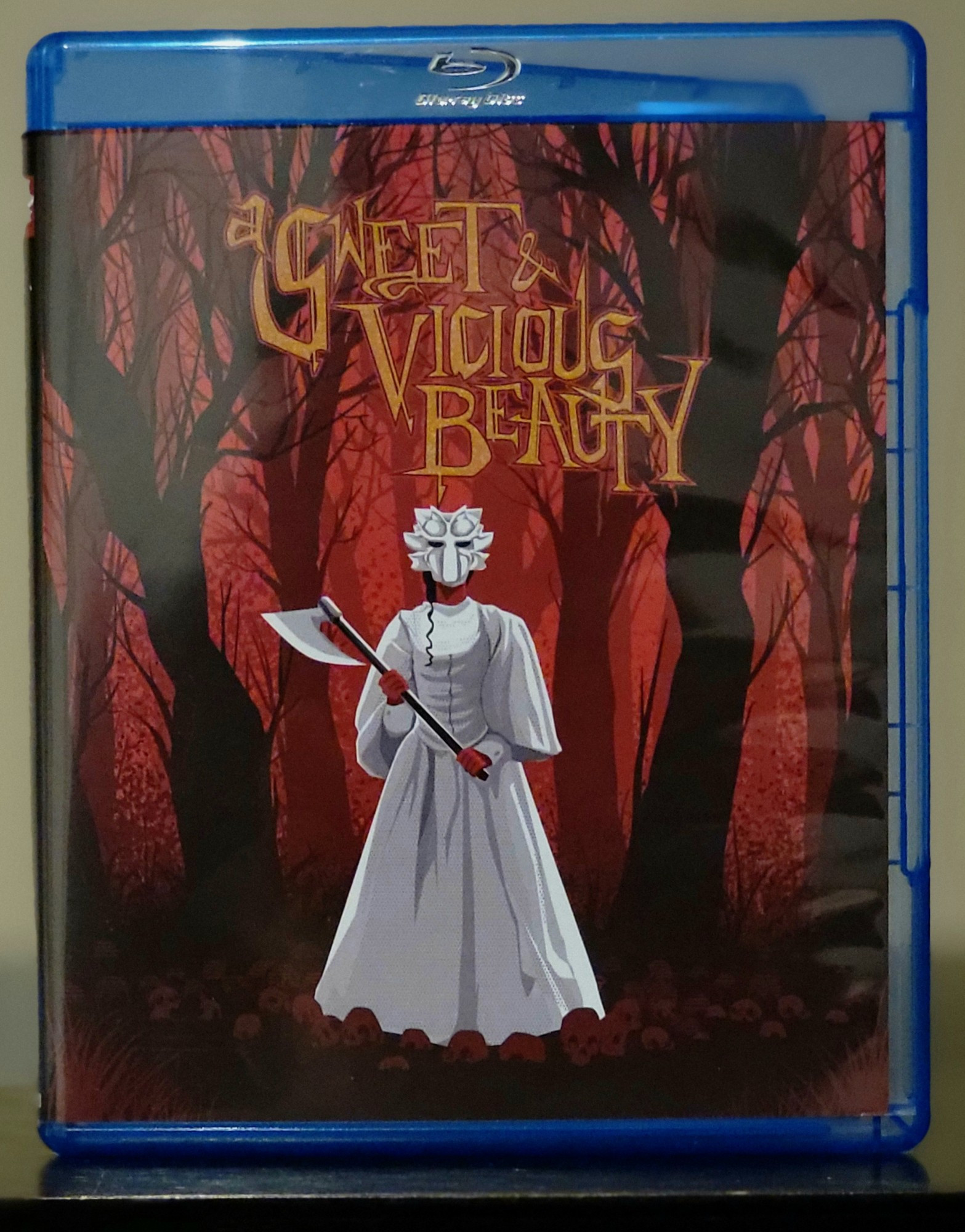 Blu ray cover for the movie A Sweet and Vicious Beauty. The art shows a woman in the woods, wearing a white gown and wearing a mask. She's holding a medieval axe with a long handle. 