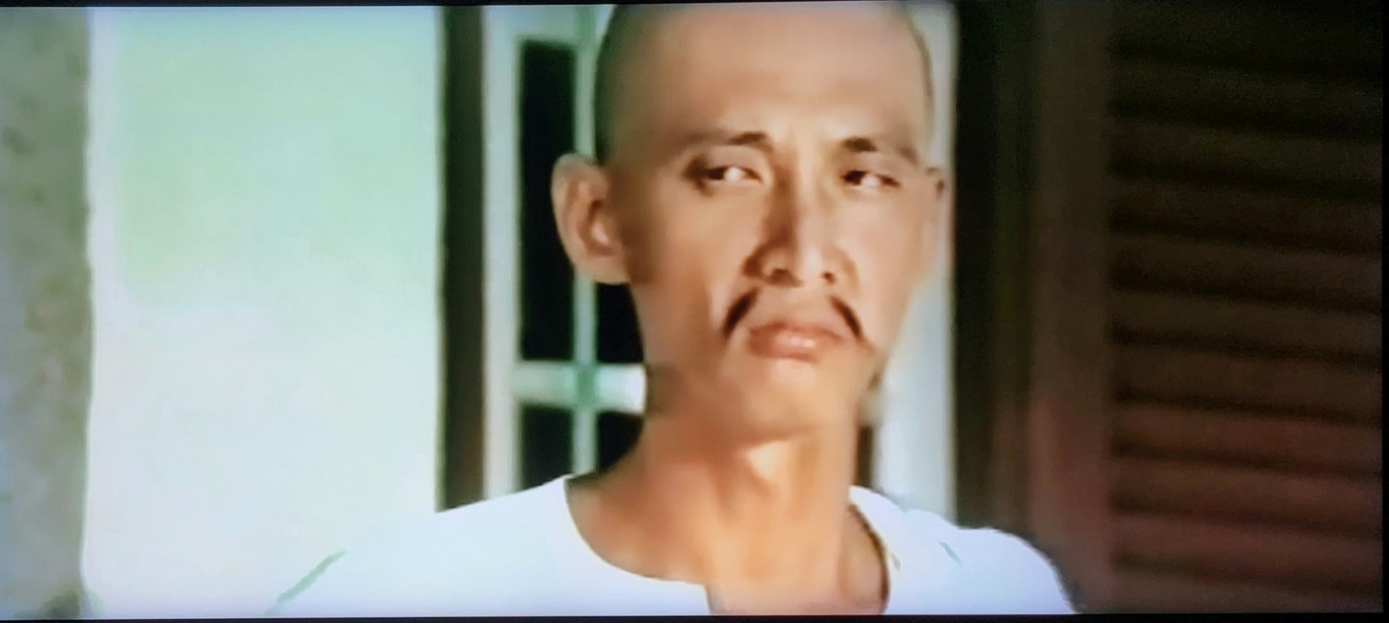 A bald man with a mustache that is two skinny wisps on either side of his face. He has a sour expression.