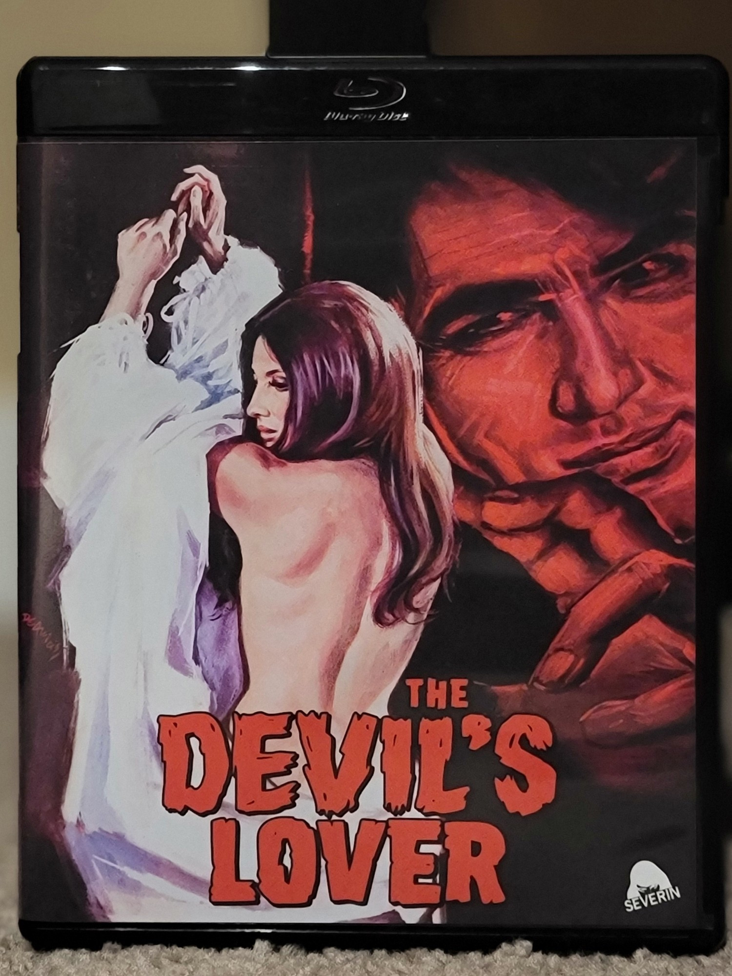 Blu ray cover for the film The Devil's Lover. The art image shows a woman partially unclothed, while a man's face is watching, reaching toward her. He is colored in red tones, suggesting the titular devil.