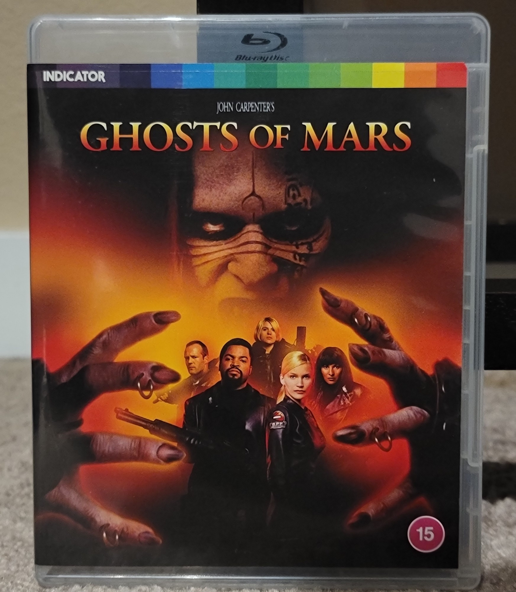 Blu ray cover for Ghosts of Mars. It shows a monster guy making a scary grabbing hand gesture and the cast is between those hands.