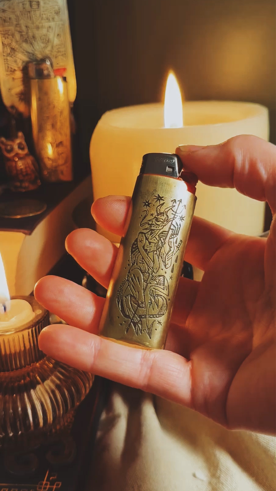 A brass lighter sleeve with a devil image etched in it being held by a hand