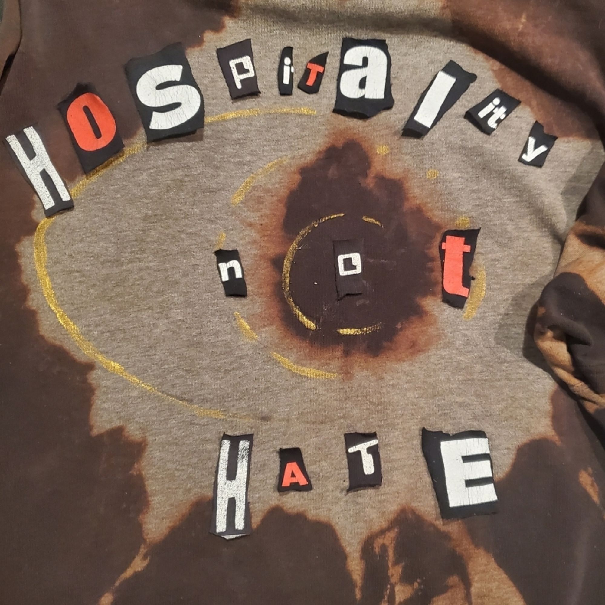 Hoodie with layout of Hospitality not Hate in scraps of letters from different shirts.