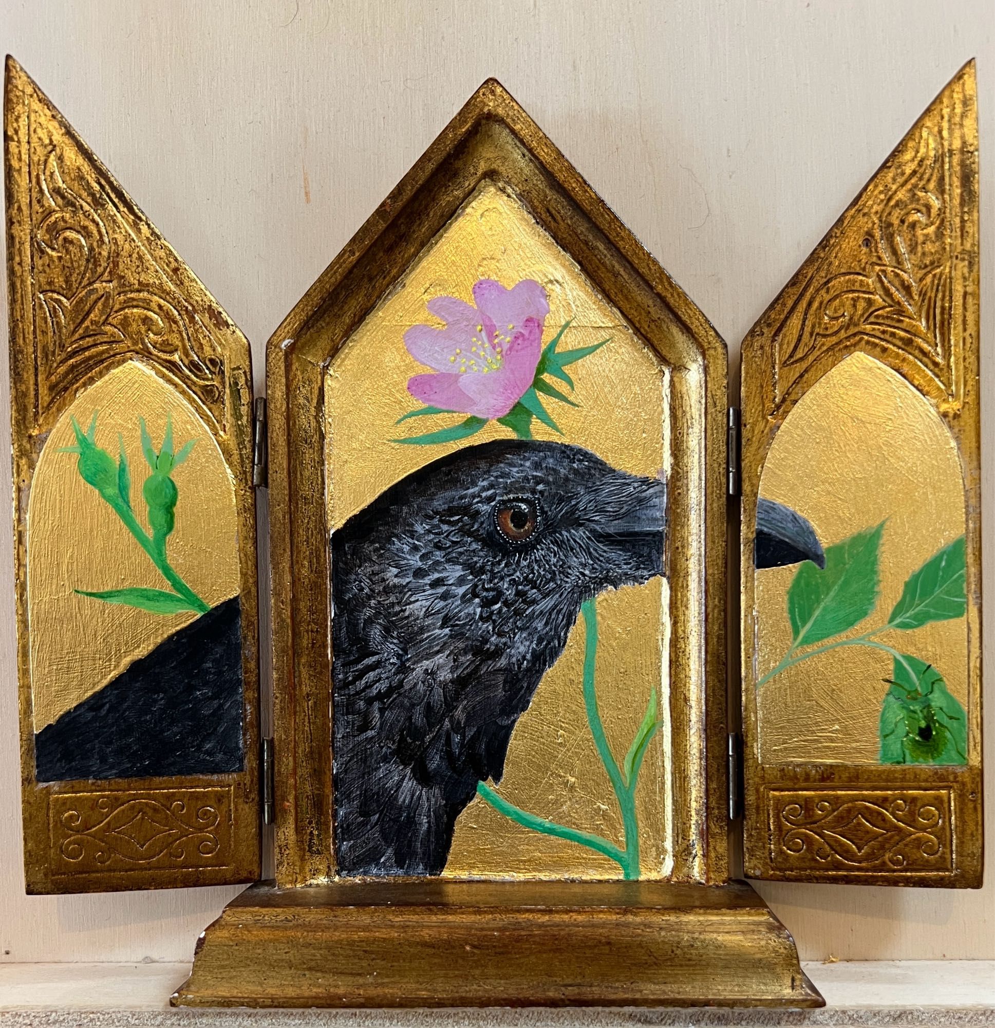 A raven walks through the wild roses looking for something to eat. A shield bug hides bottom right on a leaf. The painting is on 23 carat gold leaf laid on vintage folding panels