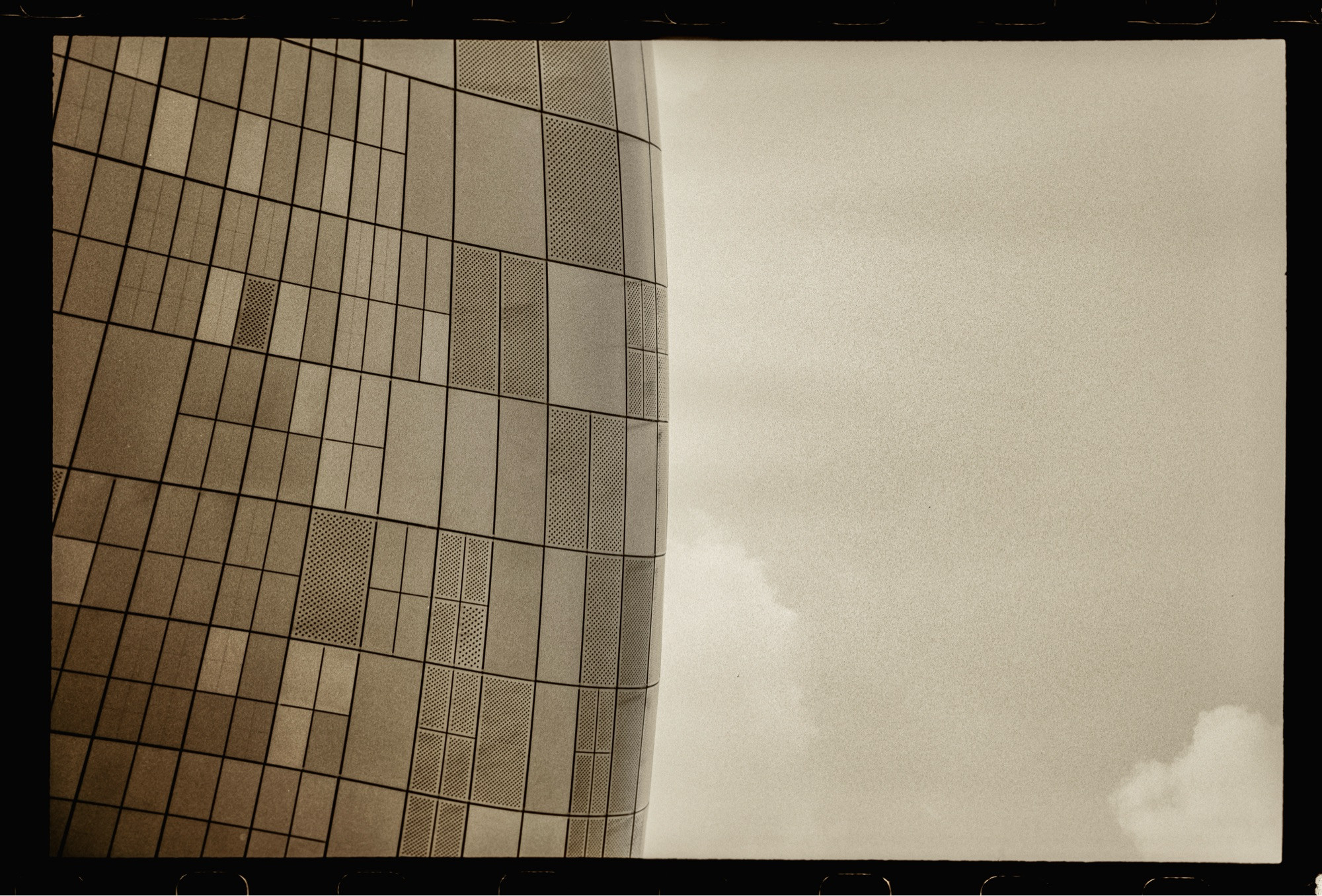 The edge of the dongdaemun design plaza building as seen from below. Lots of metal plates filling half the frame and sky filling the other.