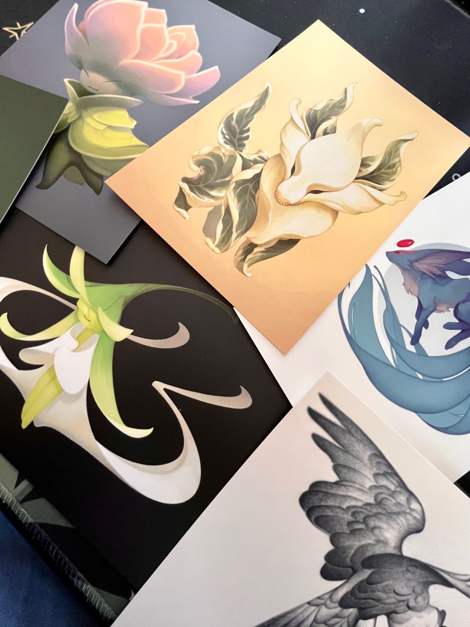 An assortment of small prints of different artwork: plantfolk, birds and carbuncles