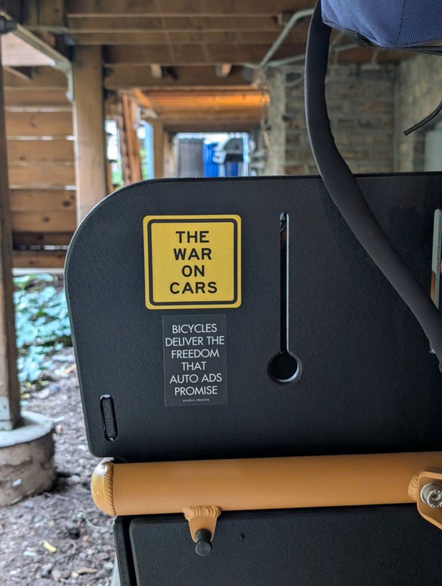 back of a cargo bike box with a yellow The War on cars sticker and a b/w sticker "Bicycles deliver the freedom that auto ads promise."