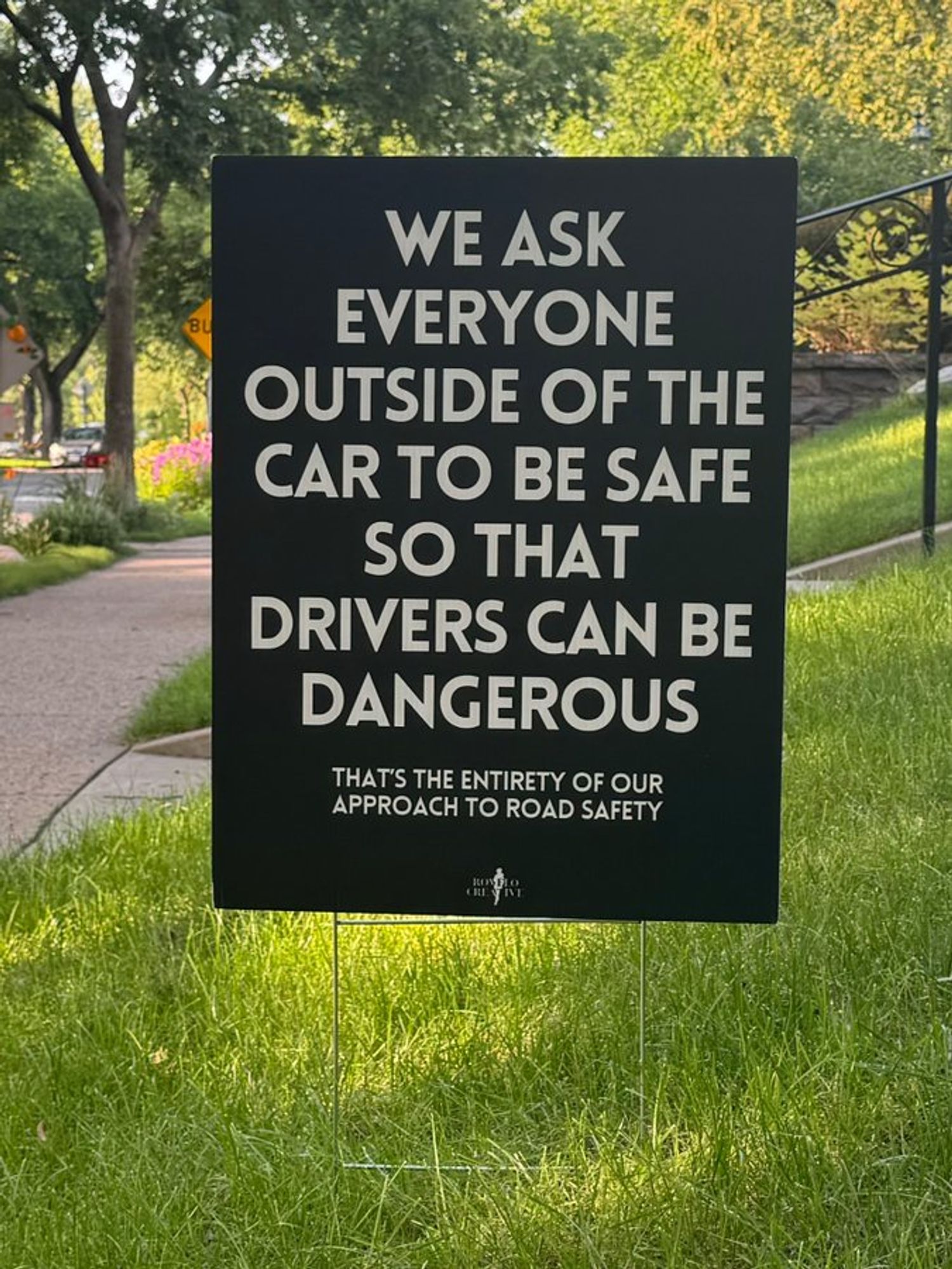 Black yard sign with white type -  we ask everyone outside of the car to be safe so that drivers can be dangerous, that's. the entirety of oru approach to road safety