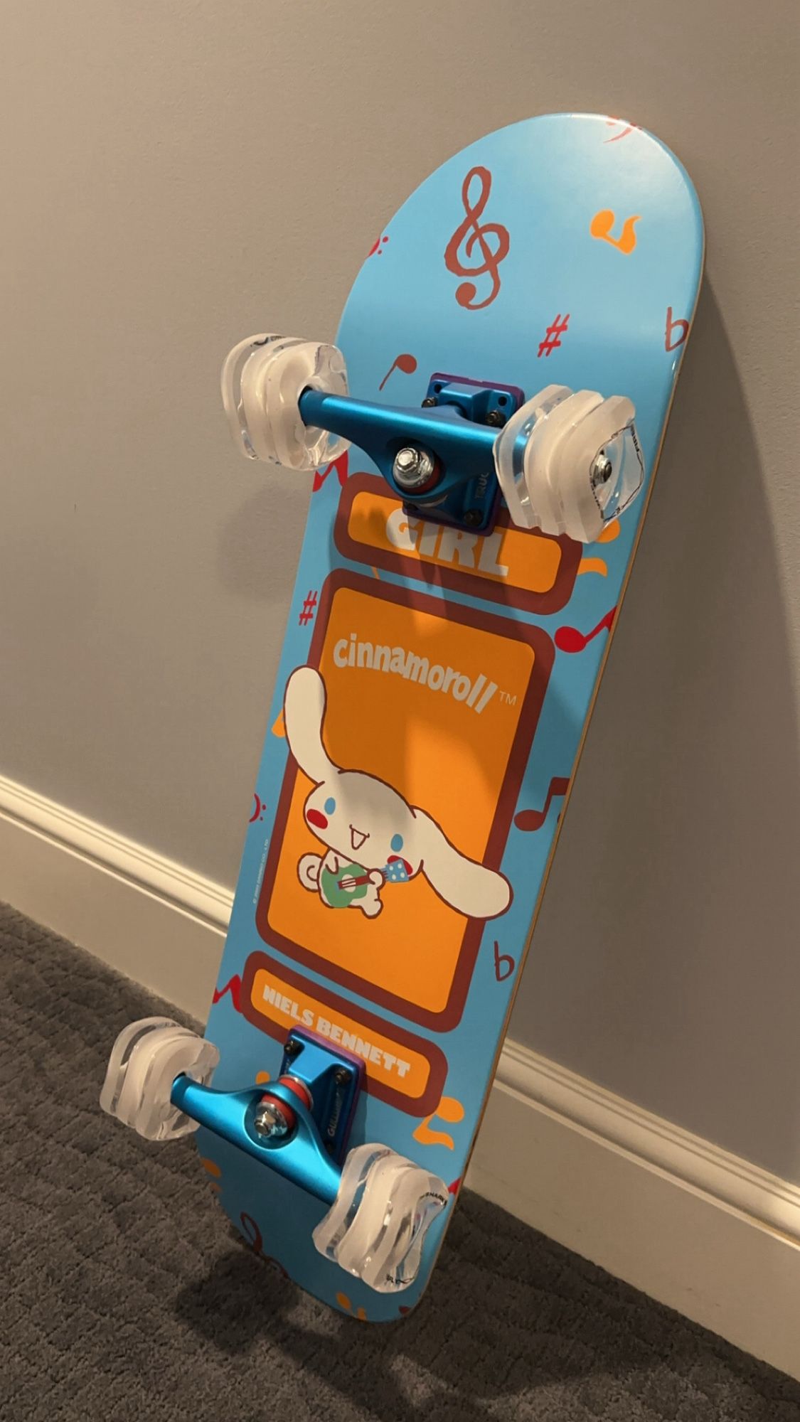 skateboard with cinnamoroll on the bottom playing a guitar. trucks are blue and wheels are funny looking and sort of square.