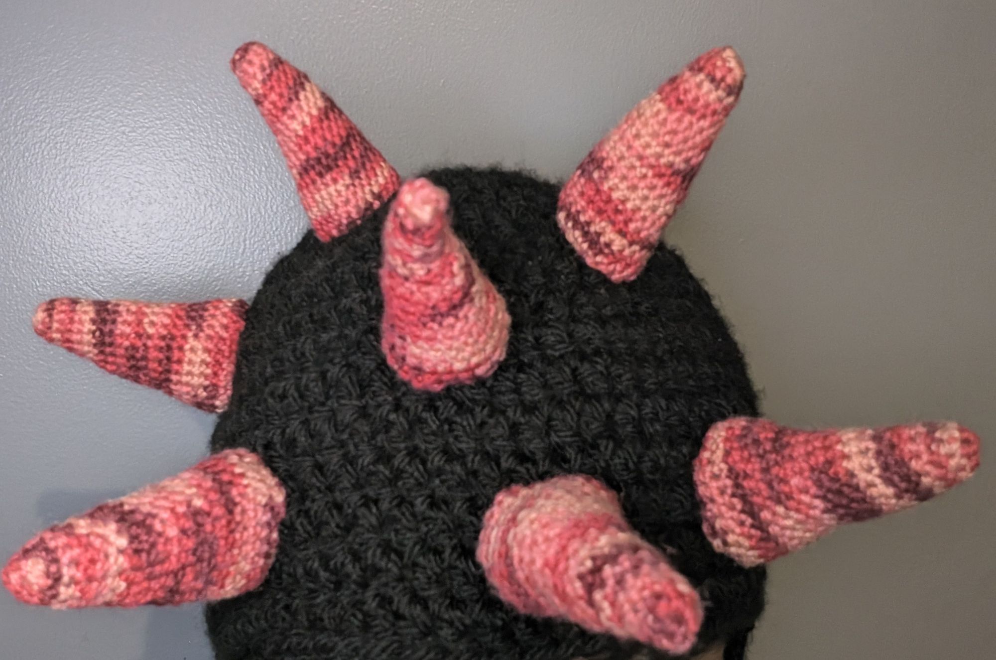 Top of a crochet balaclava in progress, with the main balaclava being black and 7 horns sewn on it, in a variegated red yarn