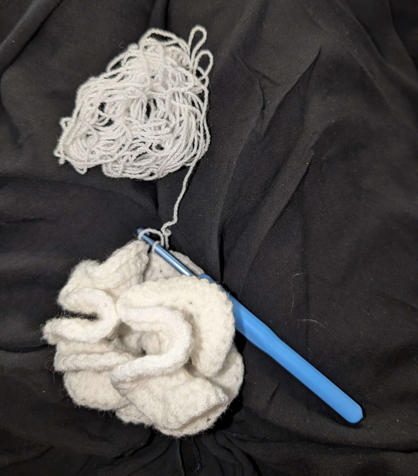 Scrunchie in white yarn with a crochet hook, and the end of a skein of white yarn connected to the scrunchie.