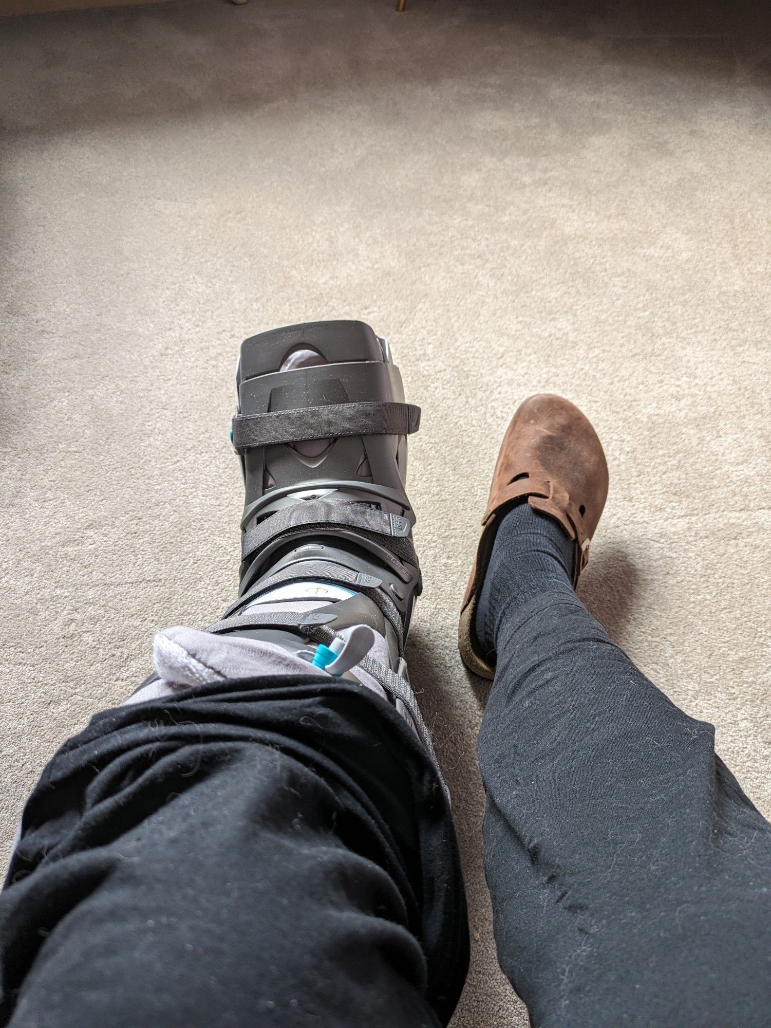 Blick auf meine Beine, der linke Fuß steckt in einem medizinischen Stiefel zur Ruhigstellung. Diagnose: Bänderriss mit knöchernen Abrissen.