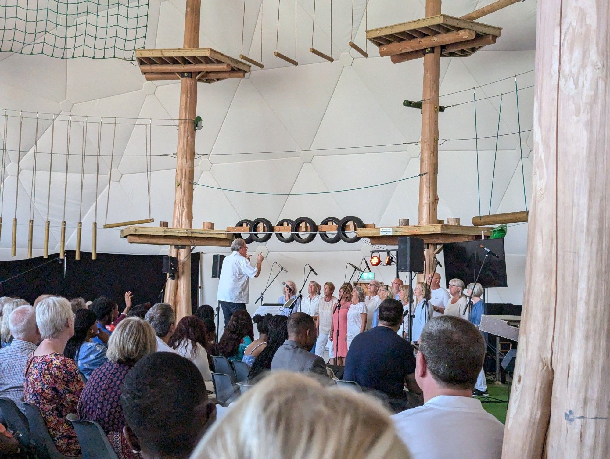 Photograph inside Let Loose Adventure Park Geodome, with congregation watching Gospel Journey choir sing. There are walkways and obstacles around the outside of the Geodome, above where the choir are singing.