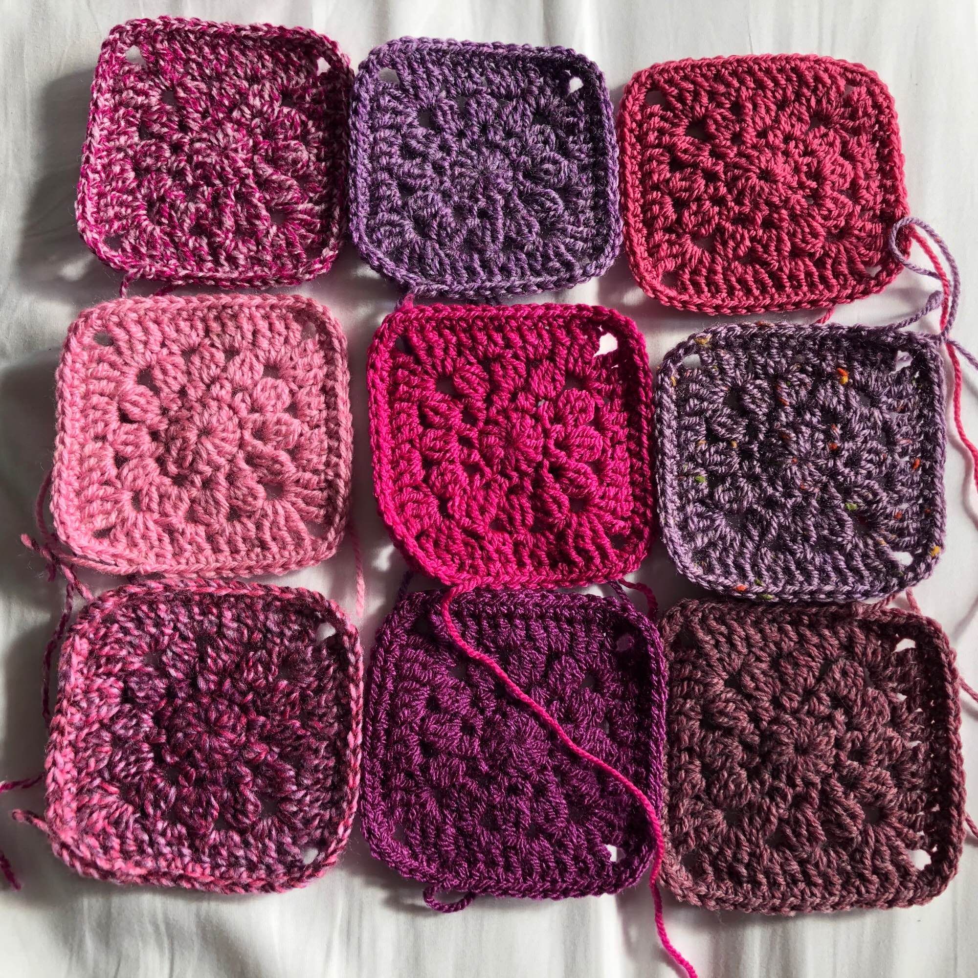 Nine crochet granny squares in various shades of pink through raspberry and magenta to purple