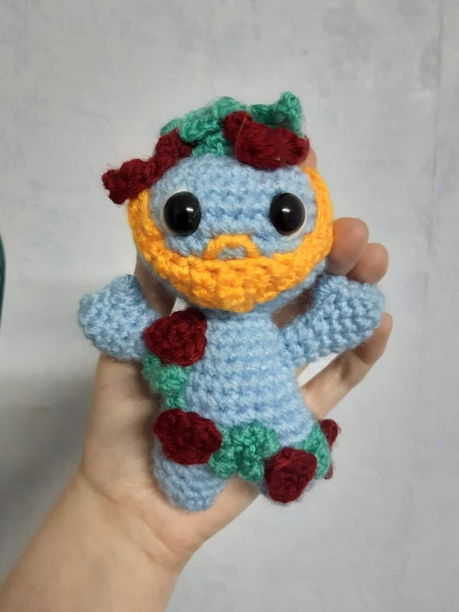 Personnage au crochet bleu tout nu. Barbe orange, guirlande et couronne de fleurs de feuilles et de raisin