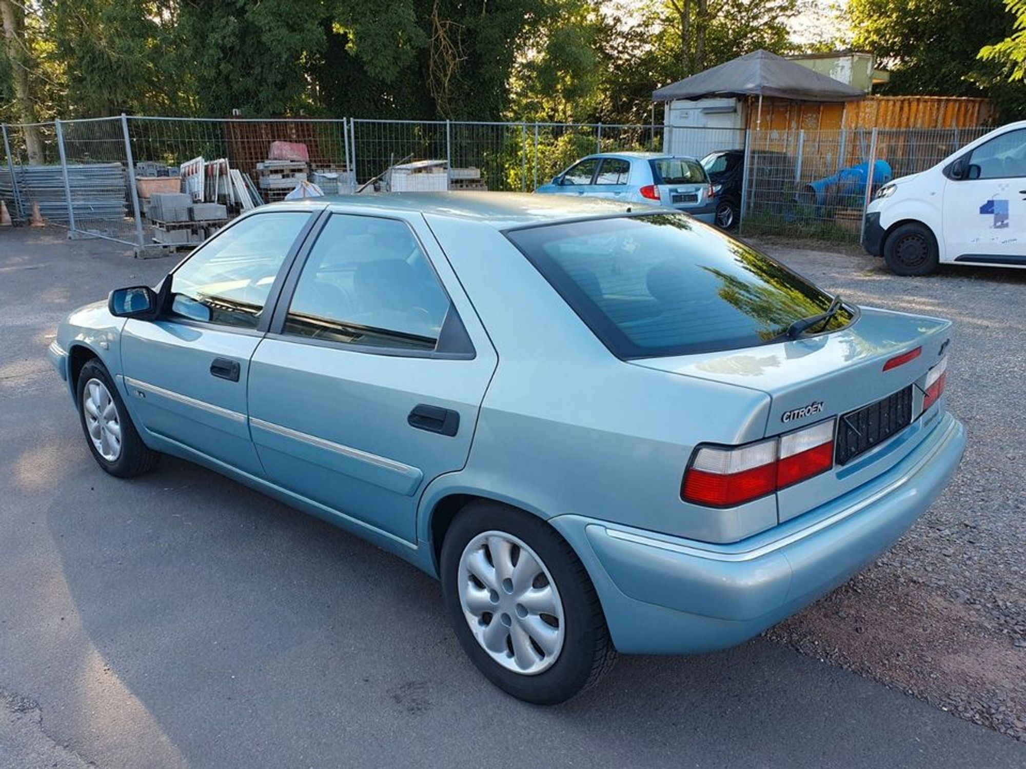 Der elegante von Bertone gestylete Viertürer in einem hellen Türkismetallic von halb hinten: leichte Keilform von der flachen Front zum hohen Heckdeckel, breite, schräge C-Säulen, Stoßfänger und seitliche Stoßleisten in Wagenfarbe mit Chromzierleisten, rot-weiße Rückleuchten