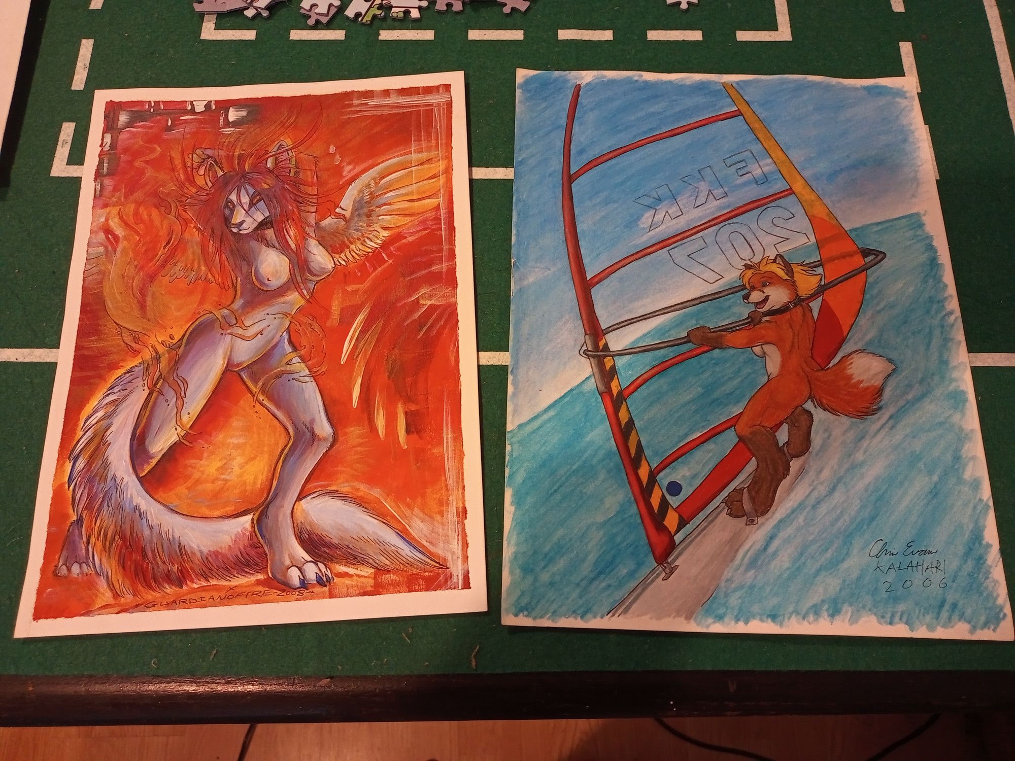 Two pieces of A4 cardstock furry art, a winged, fire-wreathed, nude canine by Guardianofire, & a nude vixen wind-surfing by Kalahari.