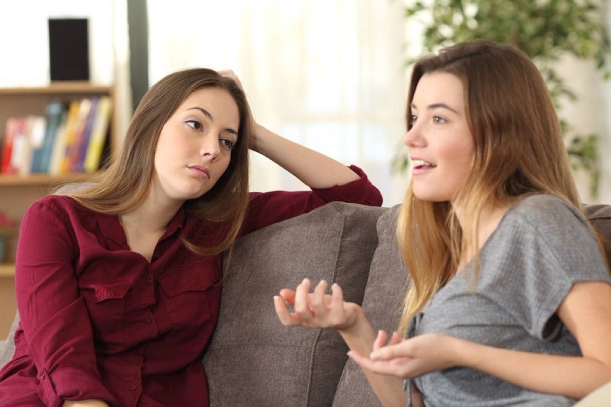 Two women on sofa, one explaining something enthusiastically while the other looks unimpressed