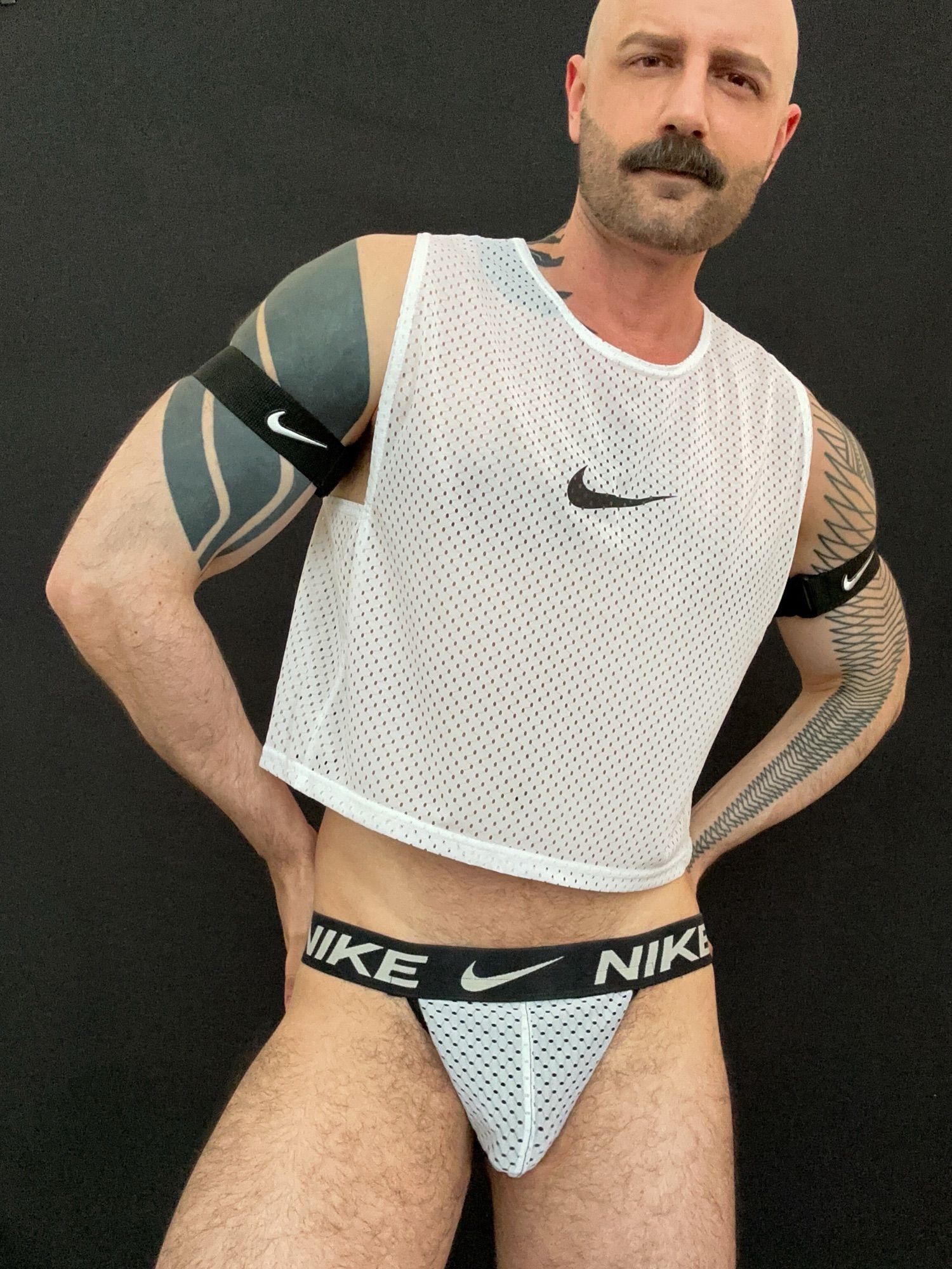 Me posing in black arm bands and a white mesh tank top and jockstrap set, all Nike branded, by Sneakermask.