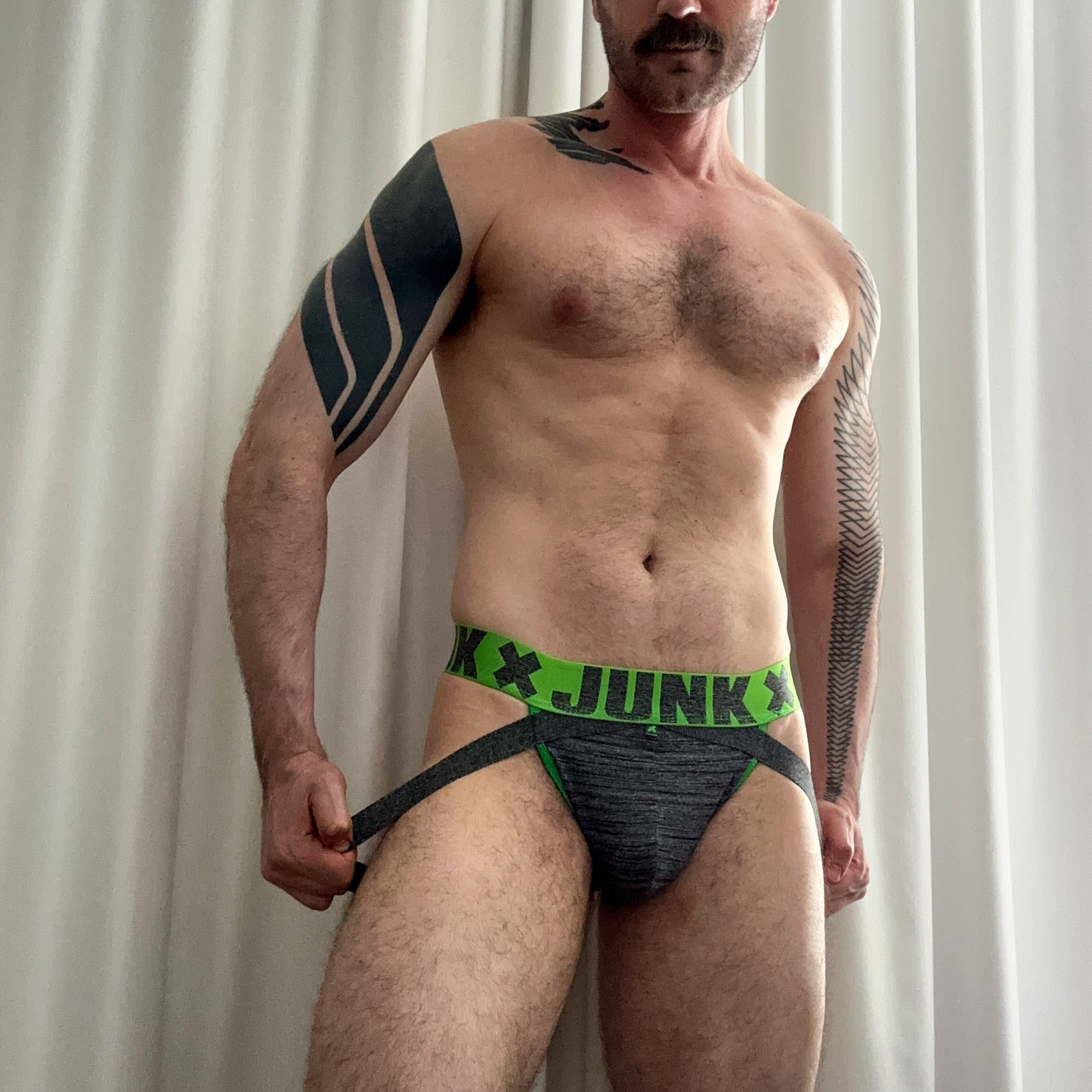 Me wearing a grey and green Junk jock in front of white drapes 