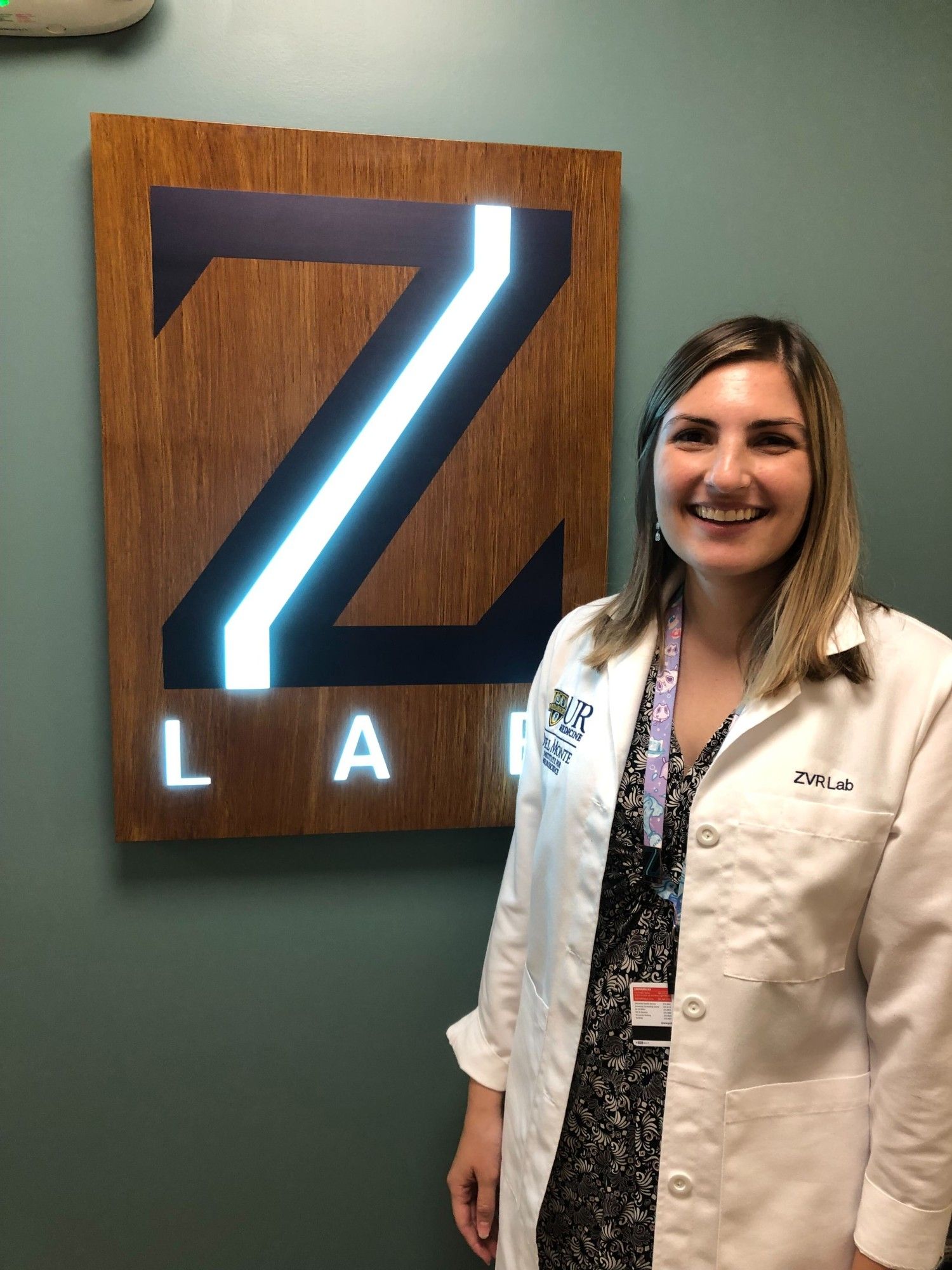 Caitlin Sharp in white lab coat stands next to Z Lab sign.