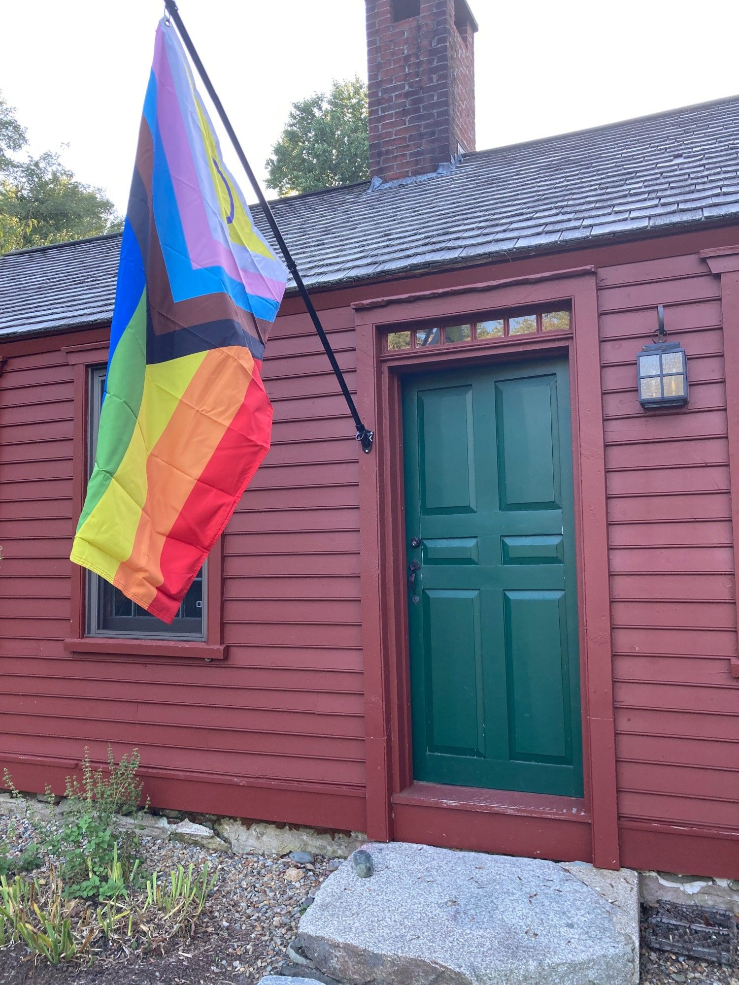 Progress pride flag hanging from a dark red house with a forest green door.