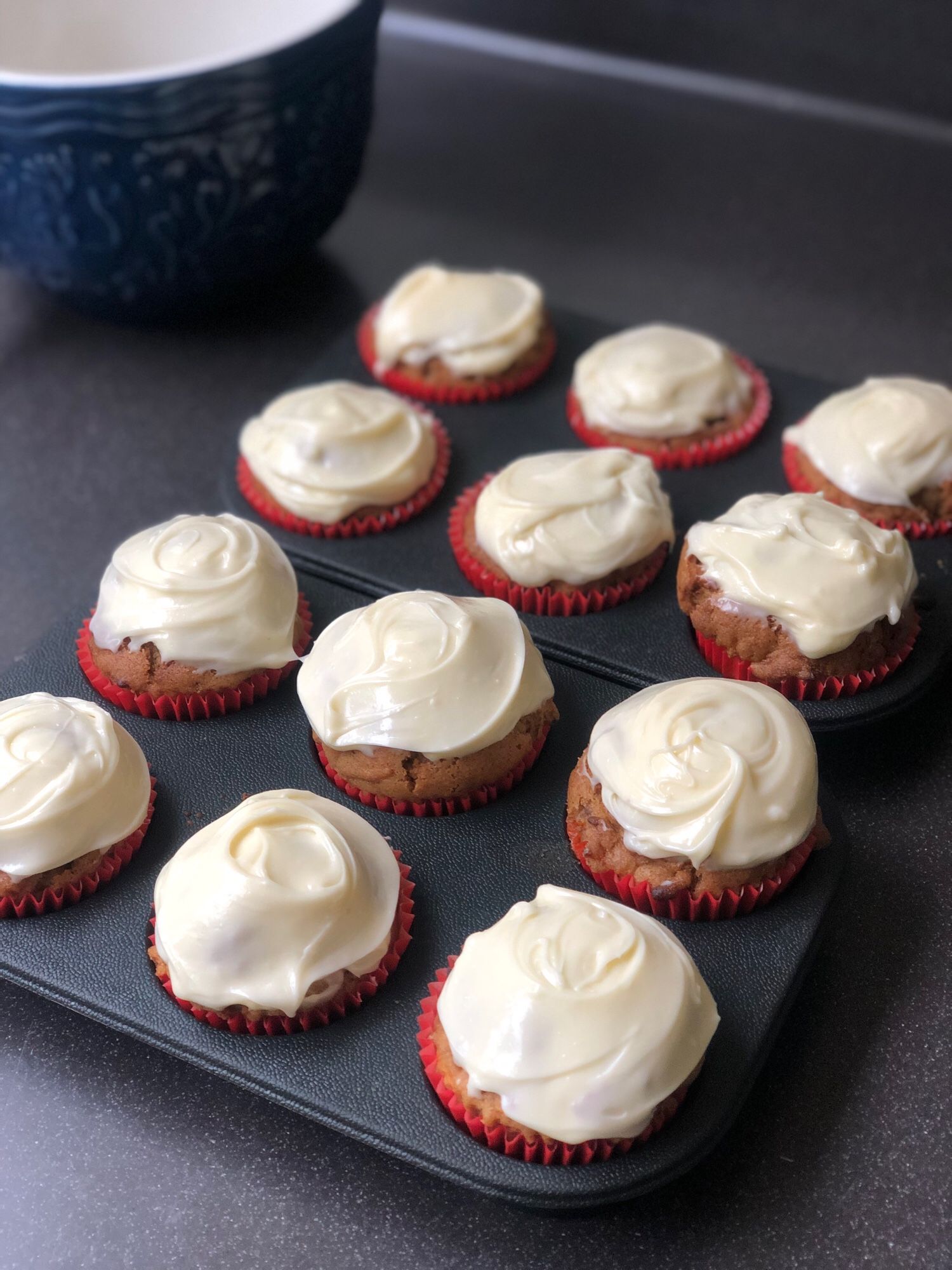 A dozen cream cheese iced muffins in blue silicone tray