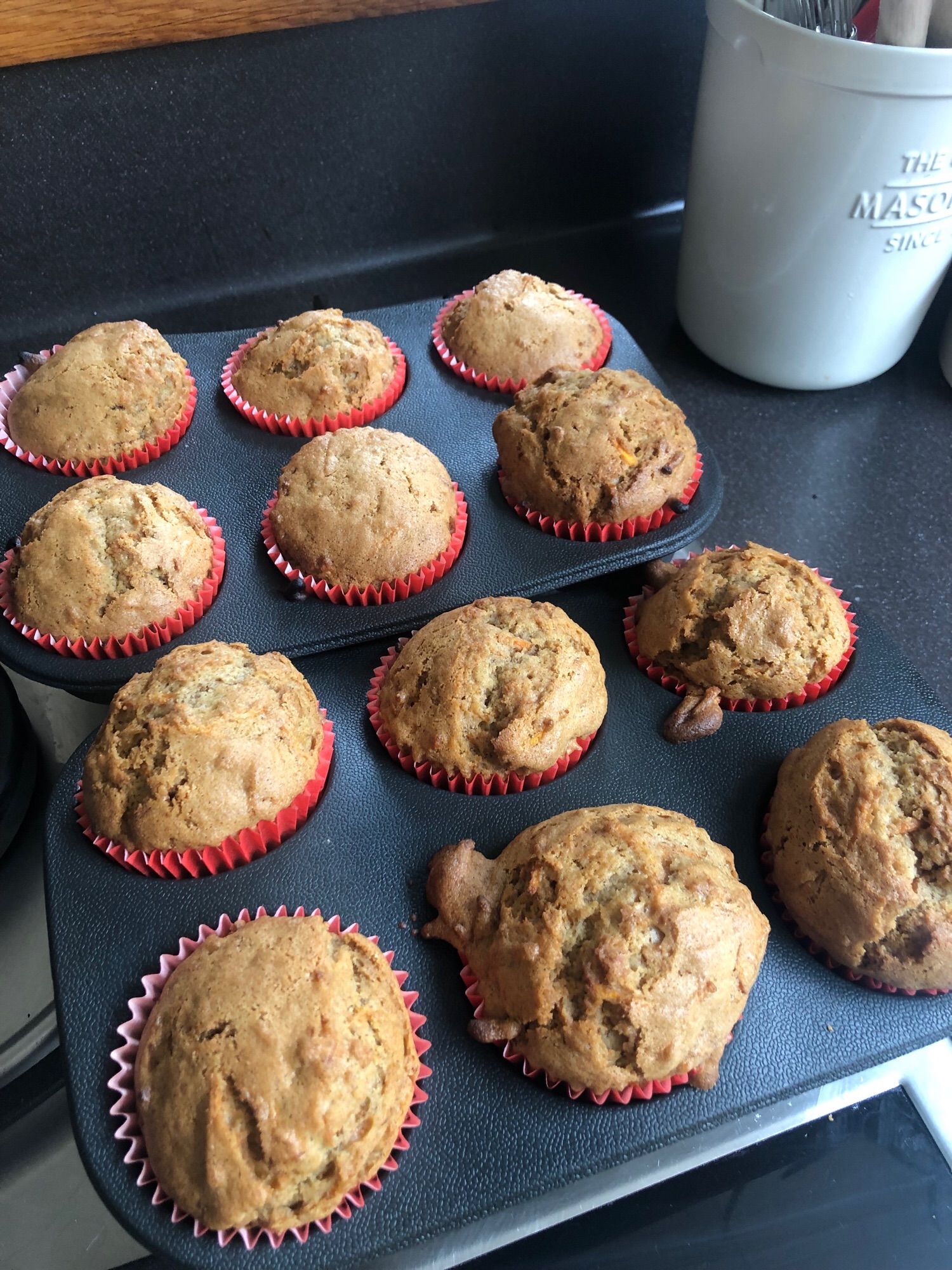 A dozen un-iced muffins in red papers in blue silicone tray