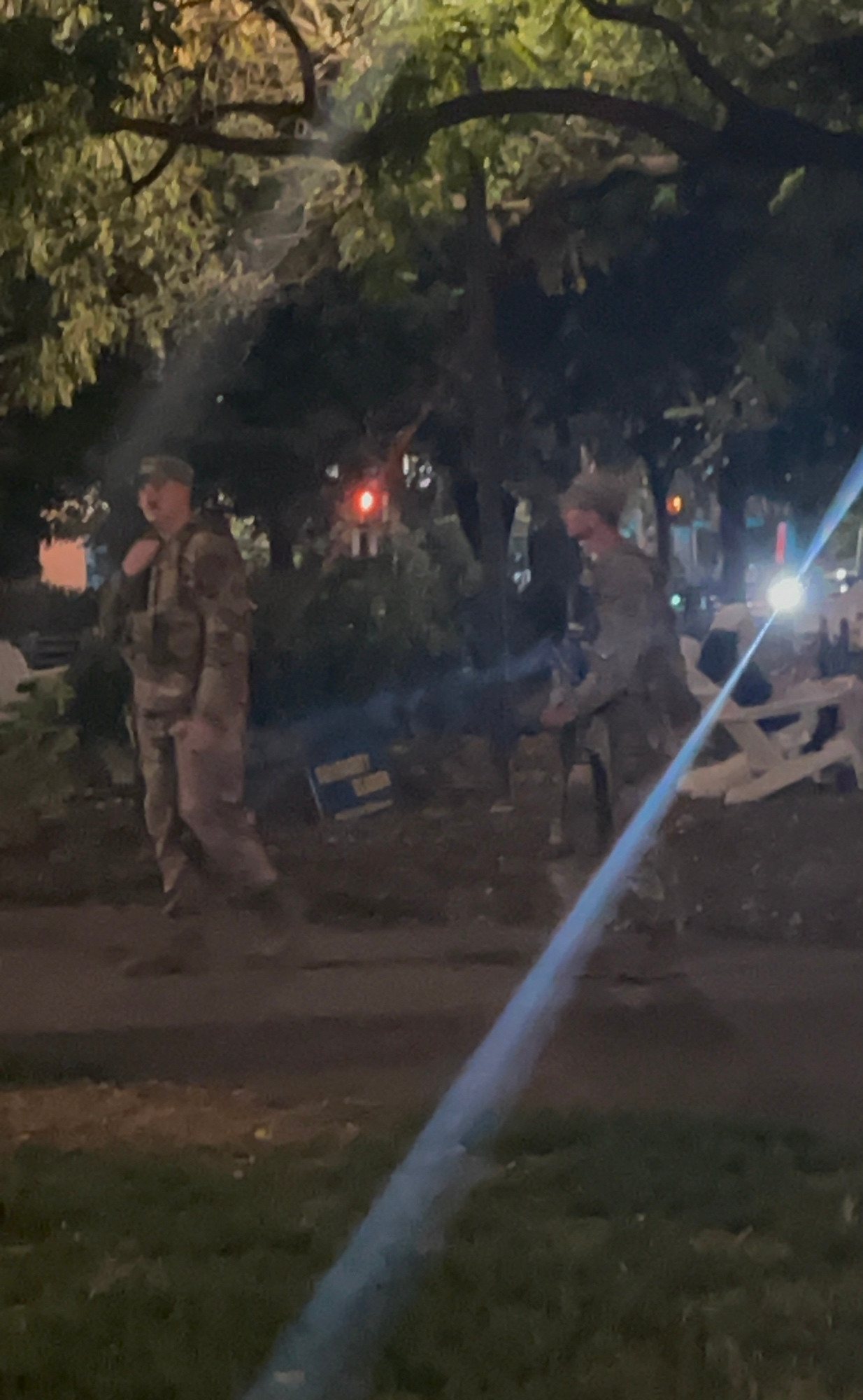 Two soldiers wandering around by the bushes in DuPont circle, one has a rifle 