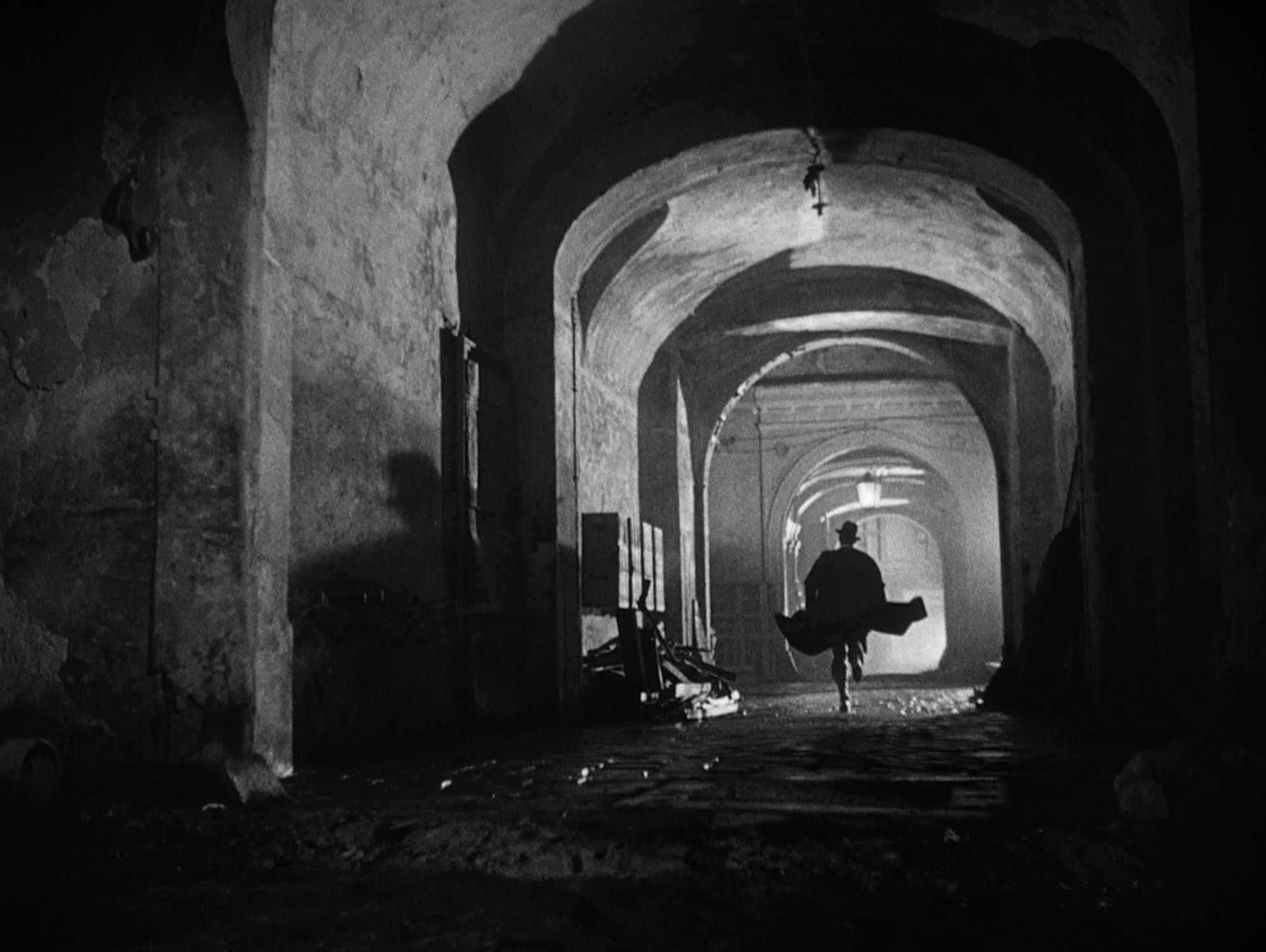 Black & white shot from the film "The third man", showing the silhouette of a man running through a tunnel in post-war Vienna, at night.