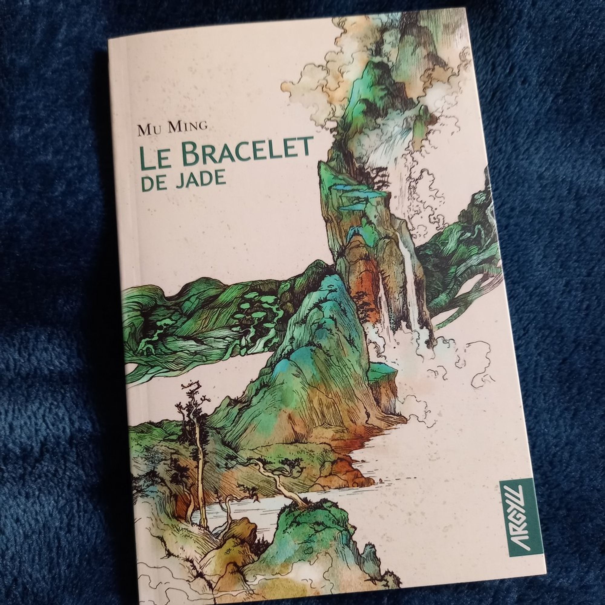 Le bracelet de jade, une novella de Mu Ming publiée dans la collection Récits aux éditions Argyll.
La couverture montre un paysage fait de montagnes et d'eau, dans des nuances de blanc et de vert, dans un style qui évoque la peinture chinoise