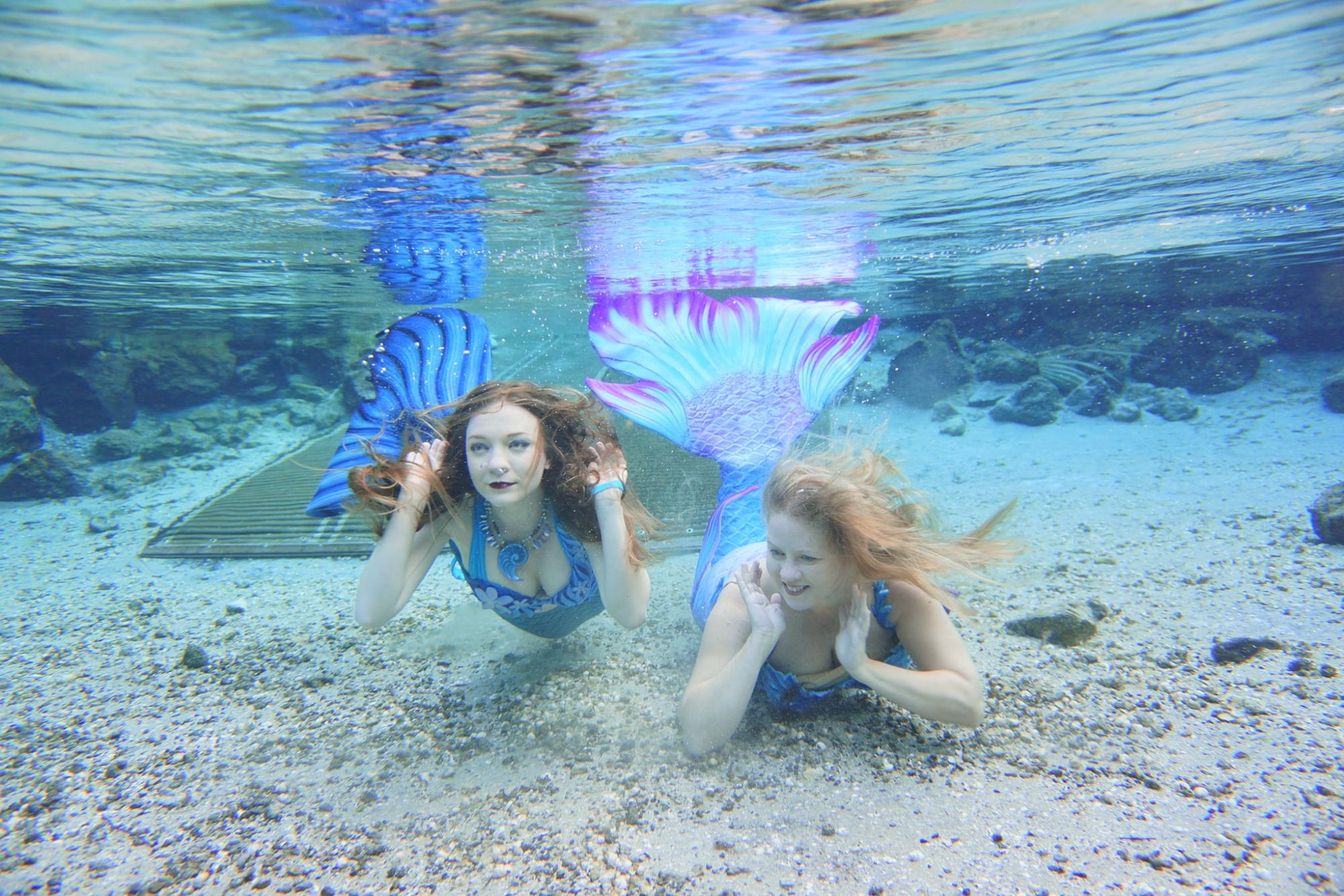 Two mermaids hanging out underwater near a boat ramp.