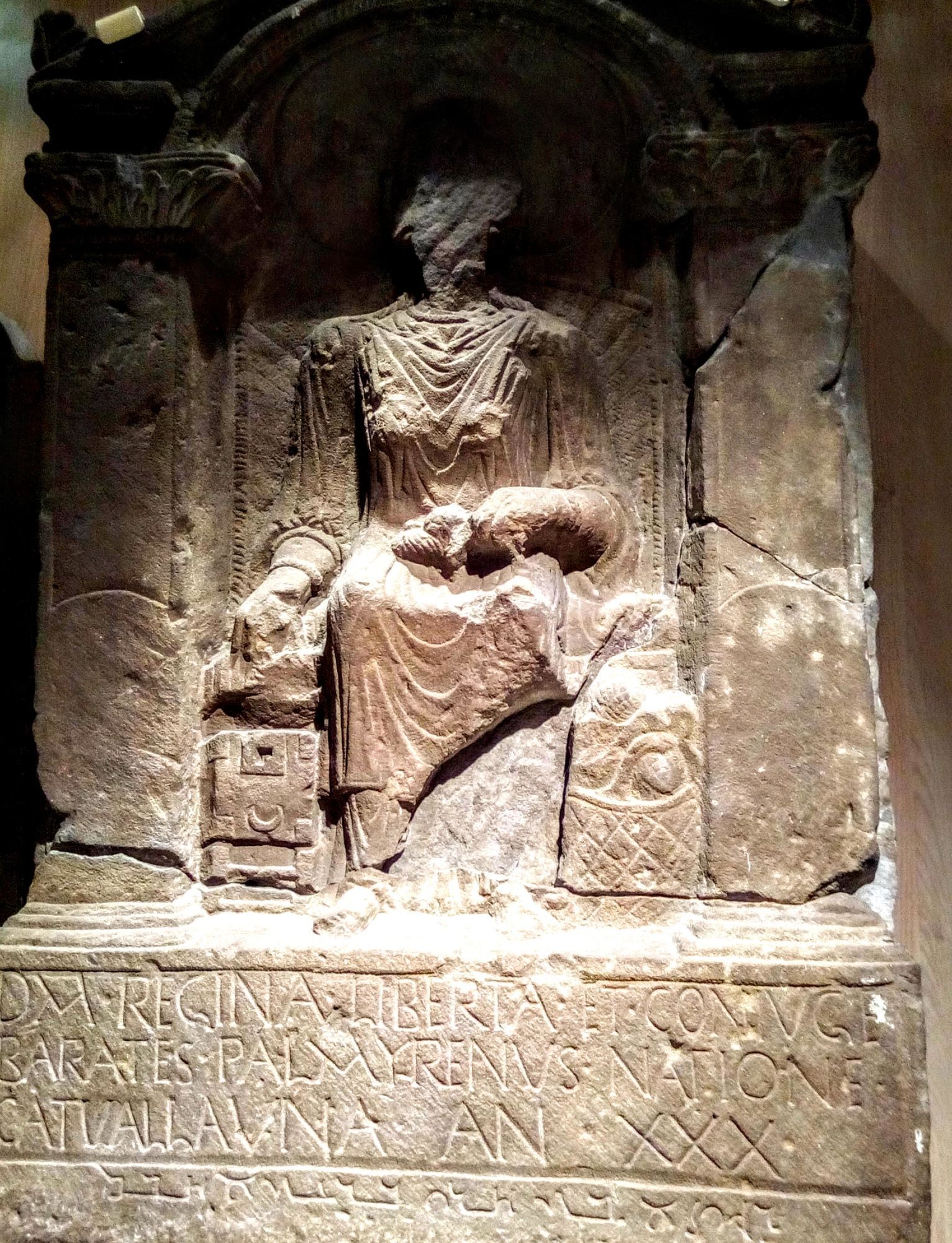 Tombstone of Regina, showing a seated figure without a face, and an inscription beneath.