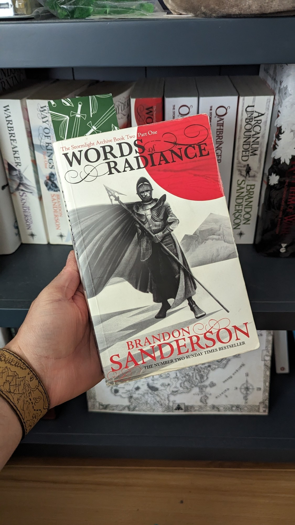 A copy of Words of Radiance by Brandon Sanderson against a backdrop of a blue bookshelf.