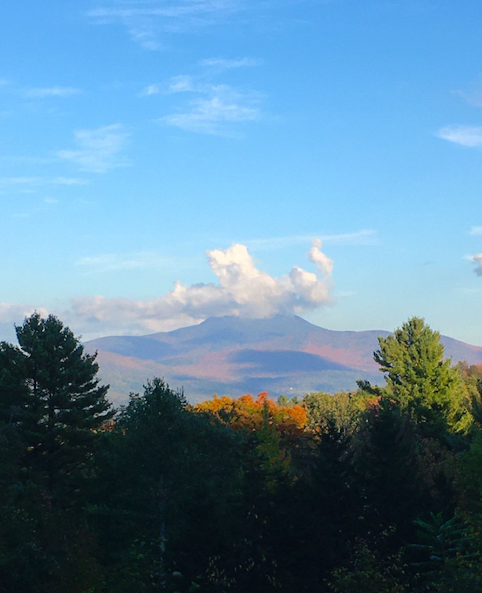 the Camel’s Hump in Vermont,  with bright fall colors showing on its flanks, and a vaguely hat-shaped cloud upon its summit.