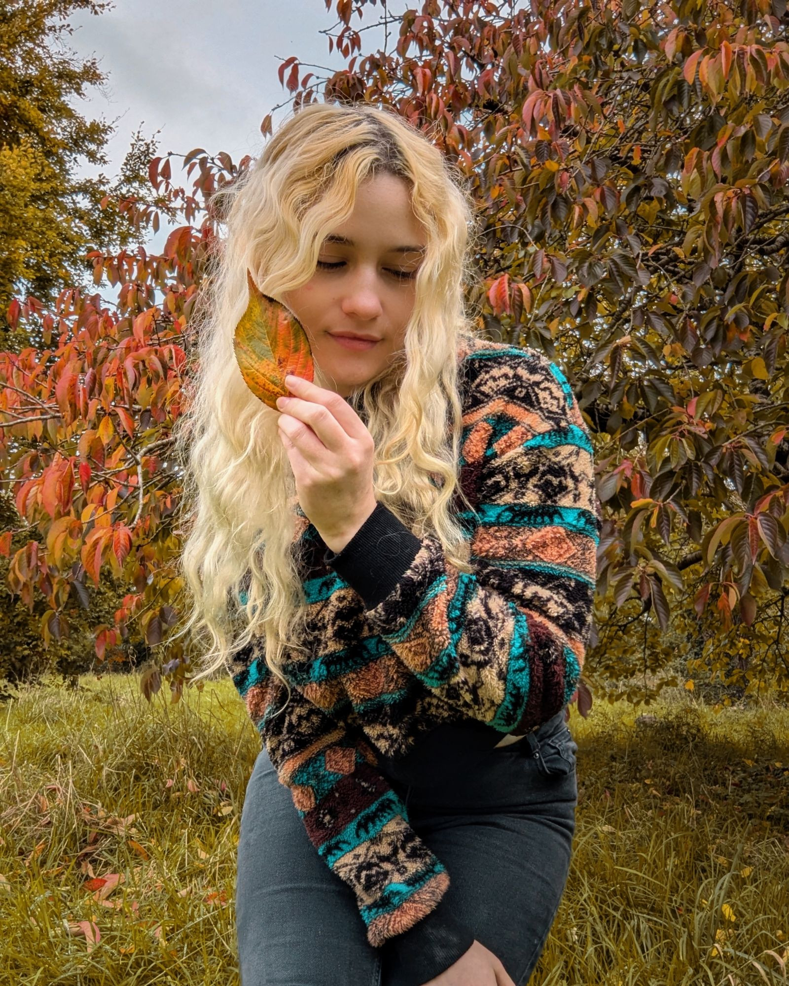 Luna outside in a busy teal black and orange jumper with autumn leaves around