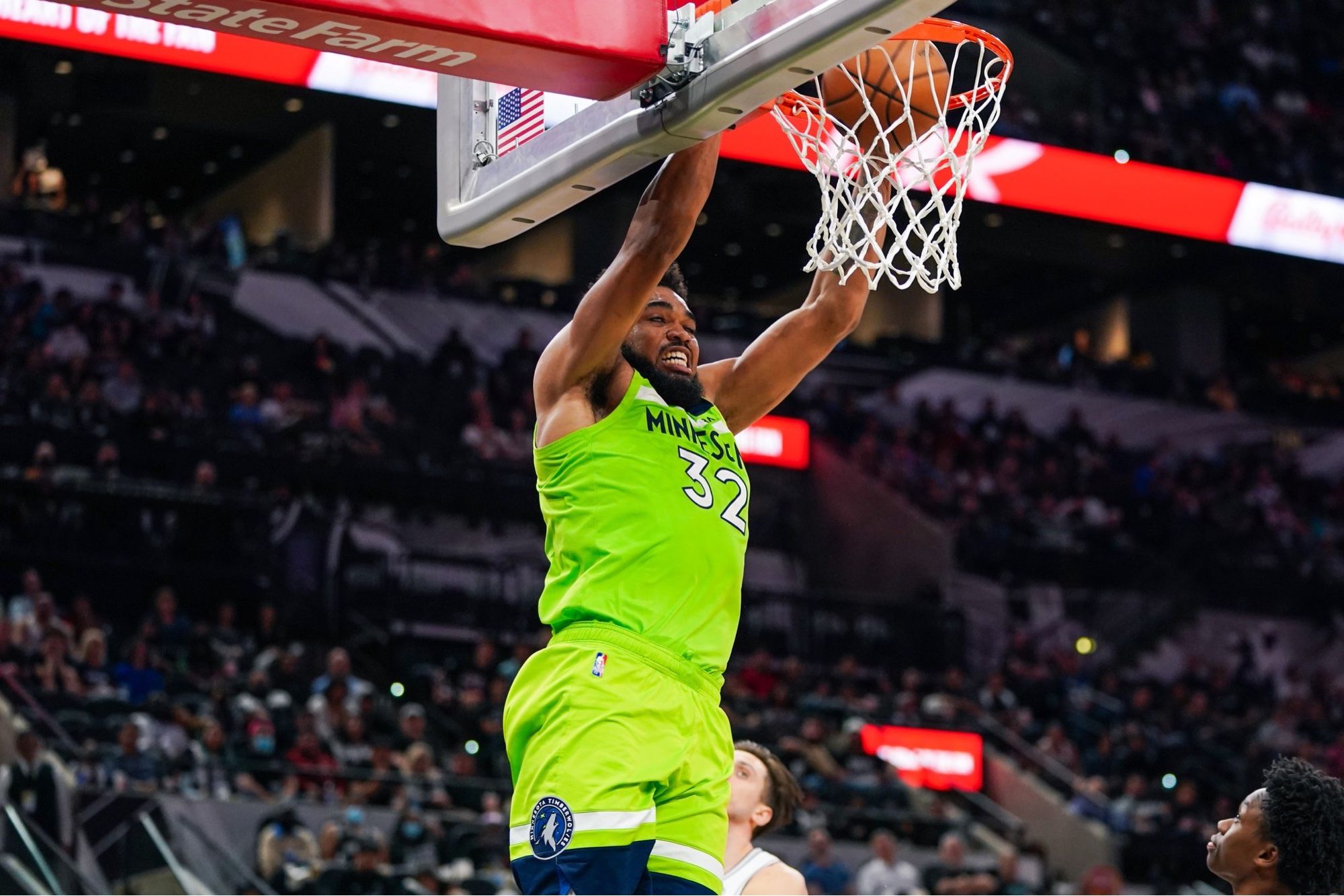 Karl-Anthony Towns dunking a basketball. He is wearing a bright green Minnesota Timberwolves uniform.