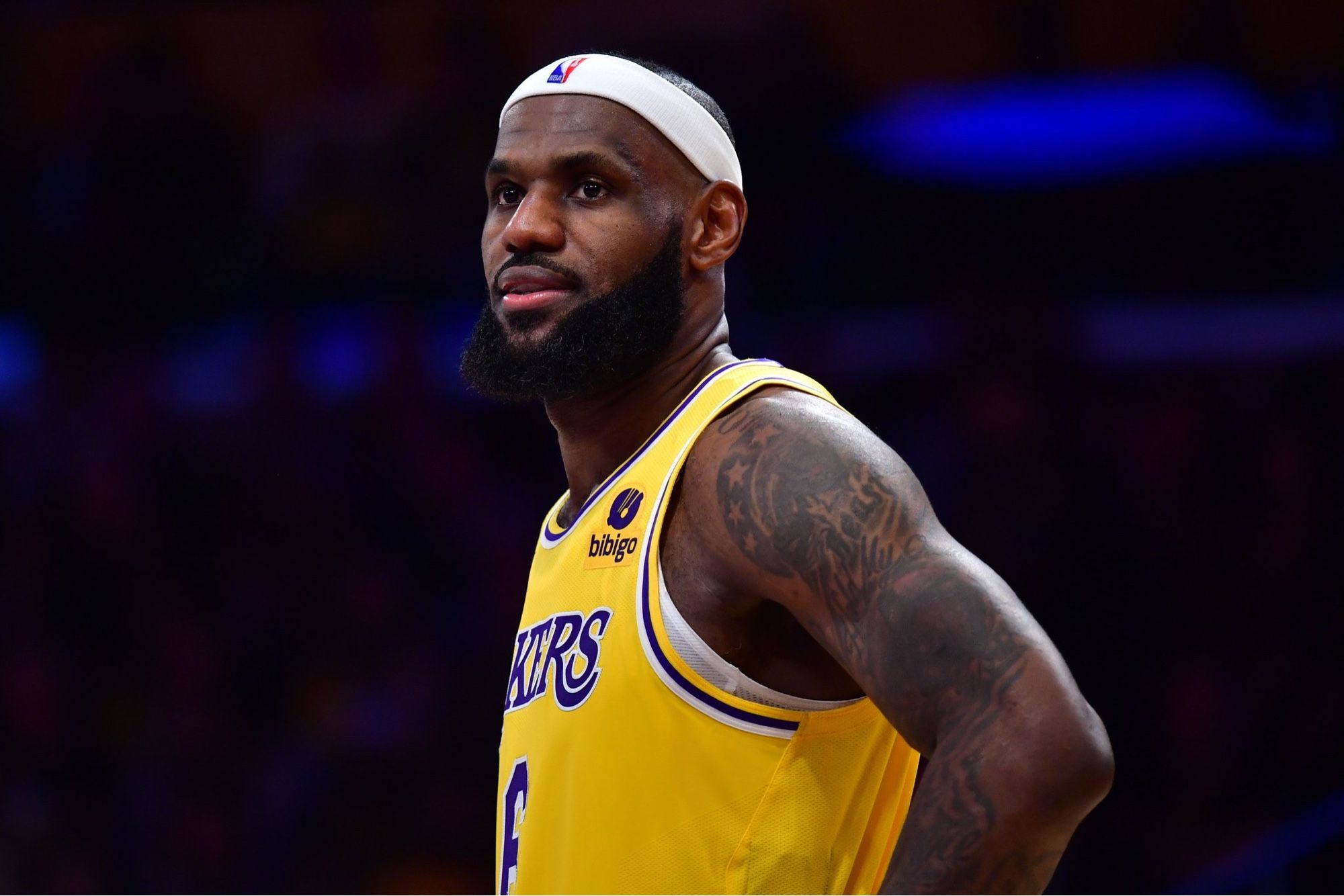 A close up of LeBron James on a basketball court. He is wearing a Lakers jersey and a white headband.