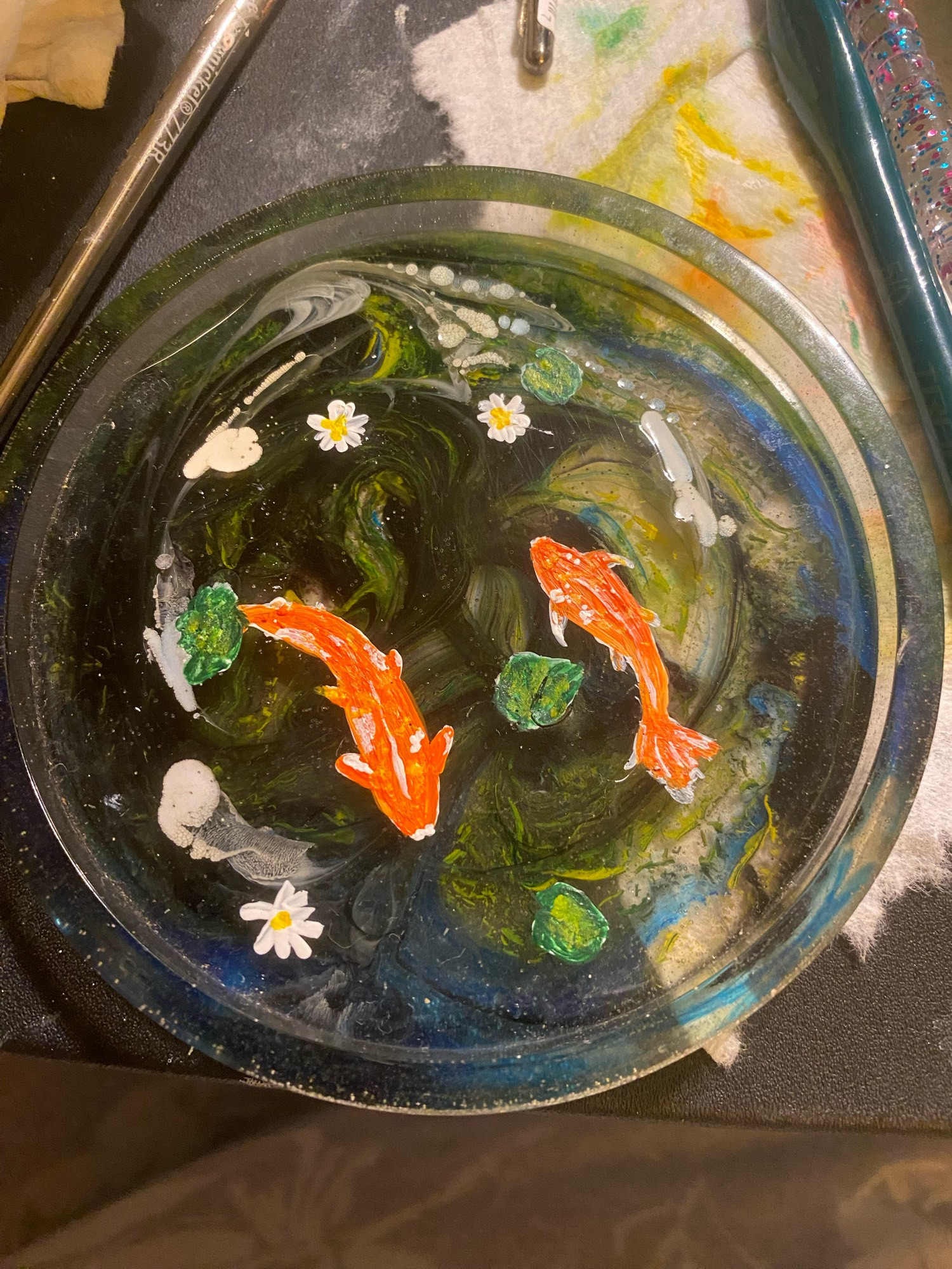 Orange and white Koi fish with green pond leaves and white with yellow center pond lilies painted in acrylic on a resin coaster.