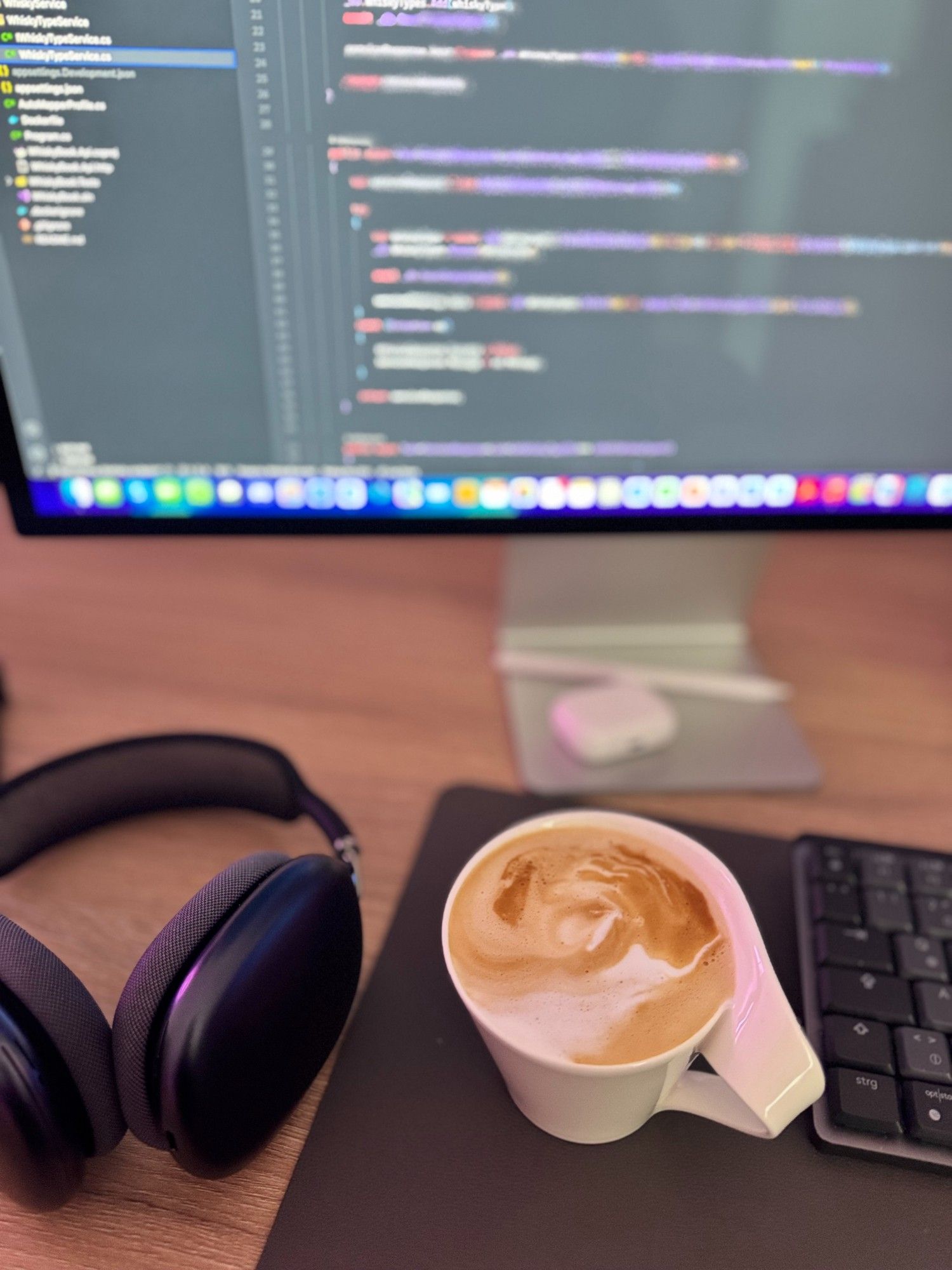 Desk with a coffee, a keyboard, AirPods Max and a coding screen.