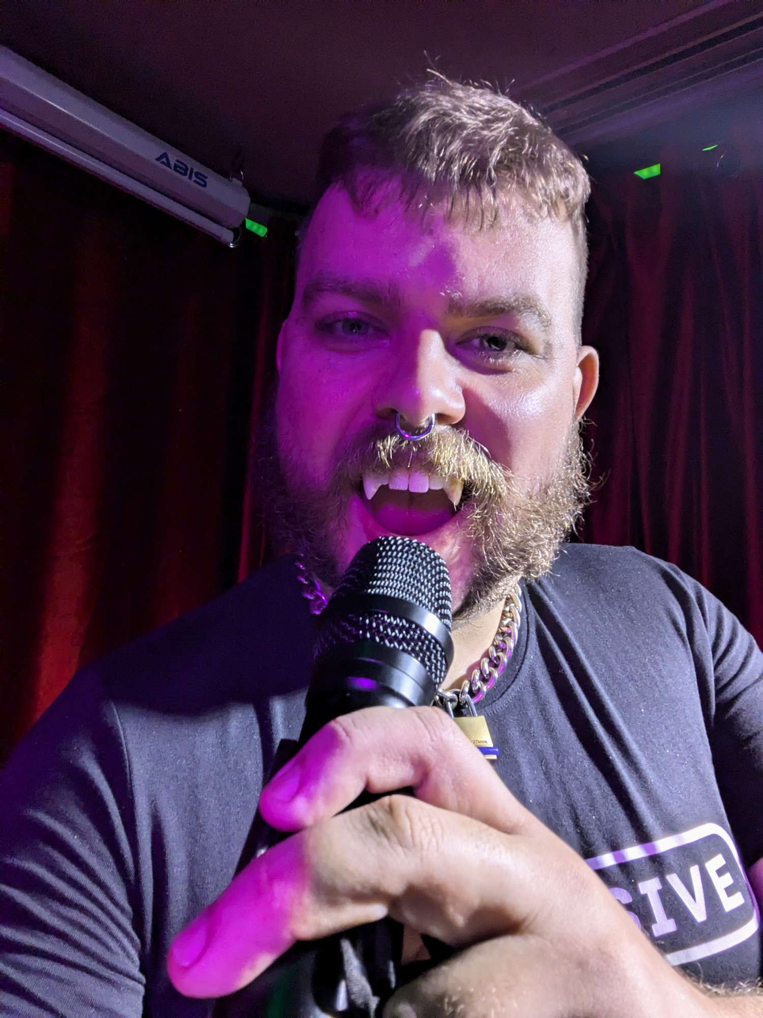 Selfie of me wearing prosthetic fangs while singing into a microphone 