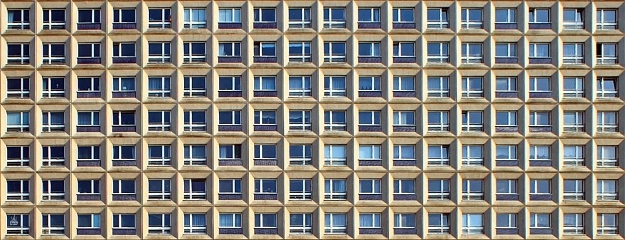 Das Bild zeigt den Teil einer Hausfassade. In 7 Reihen sind je 18 Fenster zu sehen, die alle in Beton eingefasst sind.