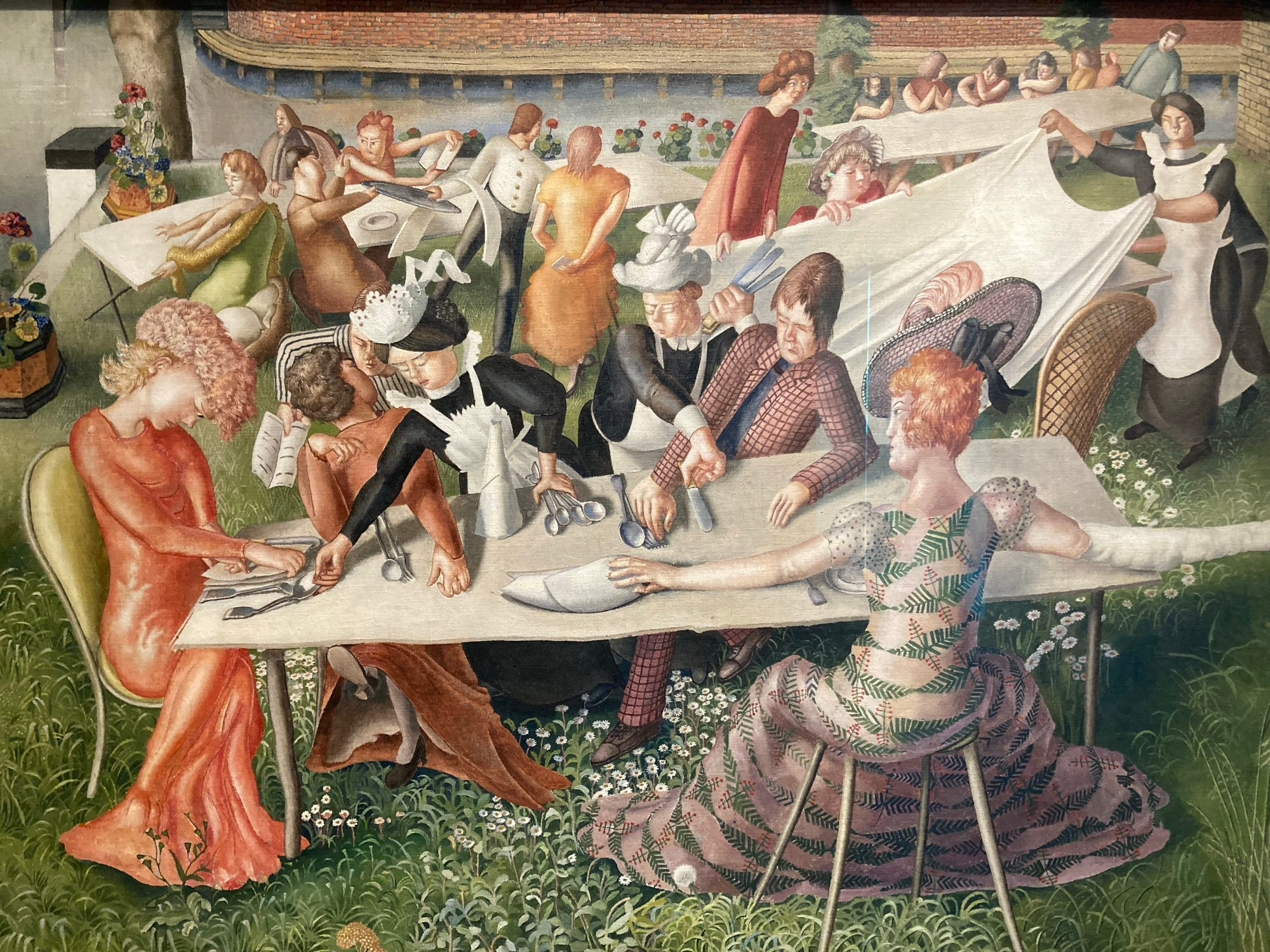 Dinner on the hotel lawn by Stanley Spencer, 1956–7. Various well-to-do guests are sitting around a table on the lawn while maids attempt to serve them. There is much activity in the background. 